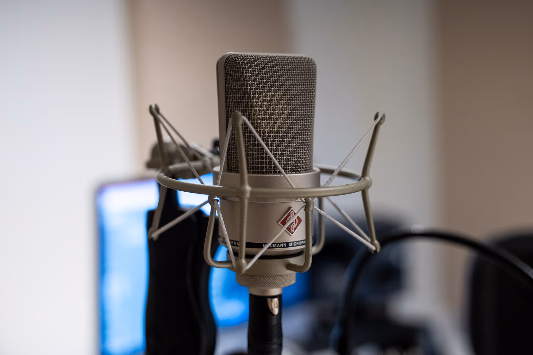 Close-up van een Neumann studiomicrofoon met popfilter en kabel in een opnameomgeving.