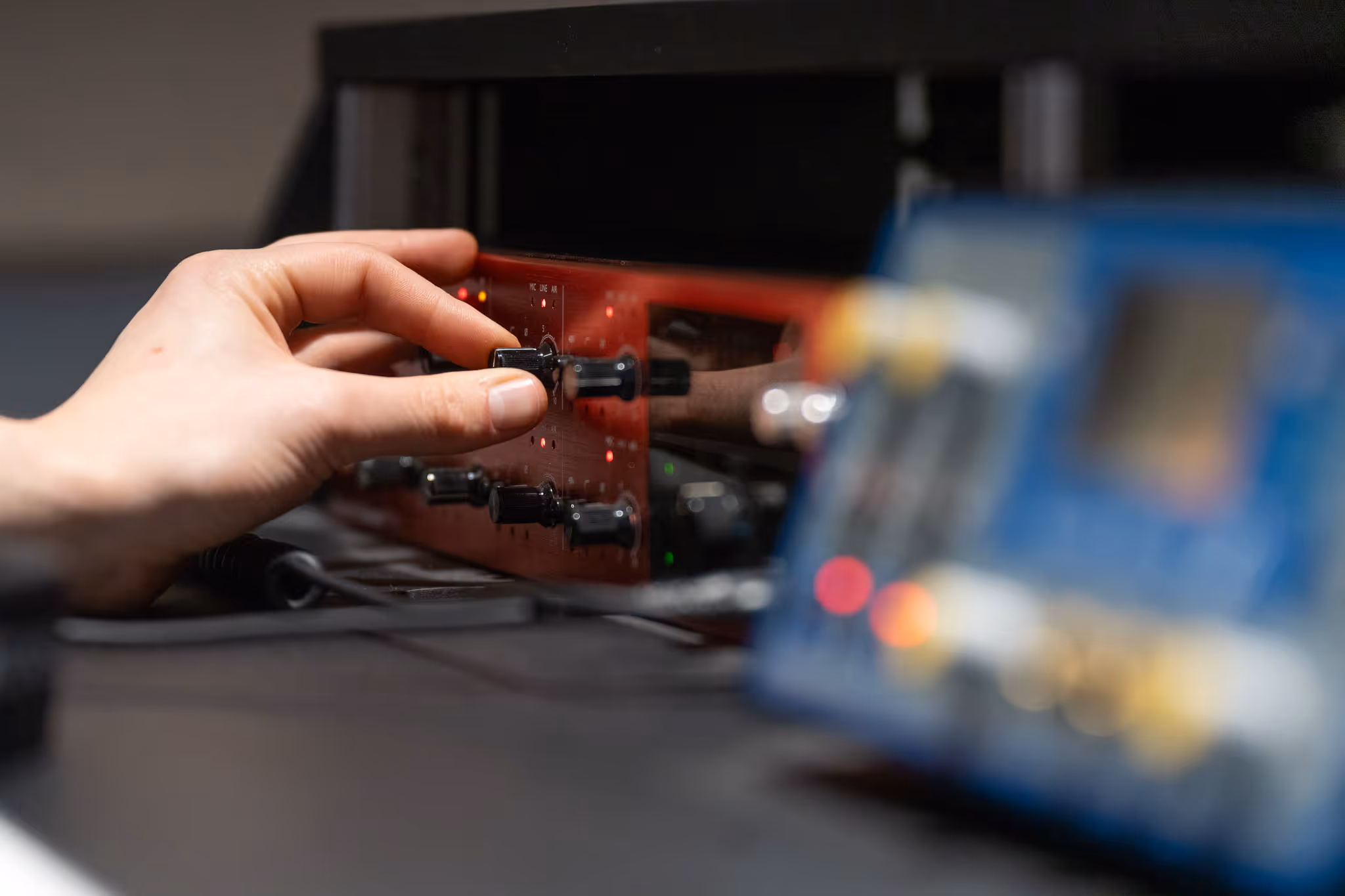 Hand die aan een knop van een rood audio-apparaat draait met een onscherp blauw apparaat op de voorgrond.