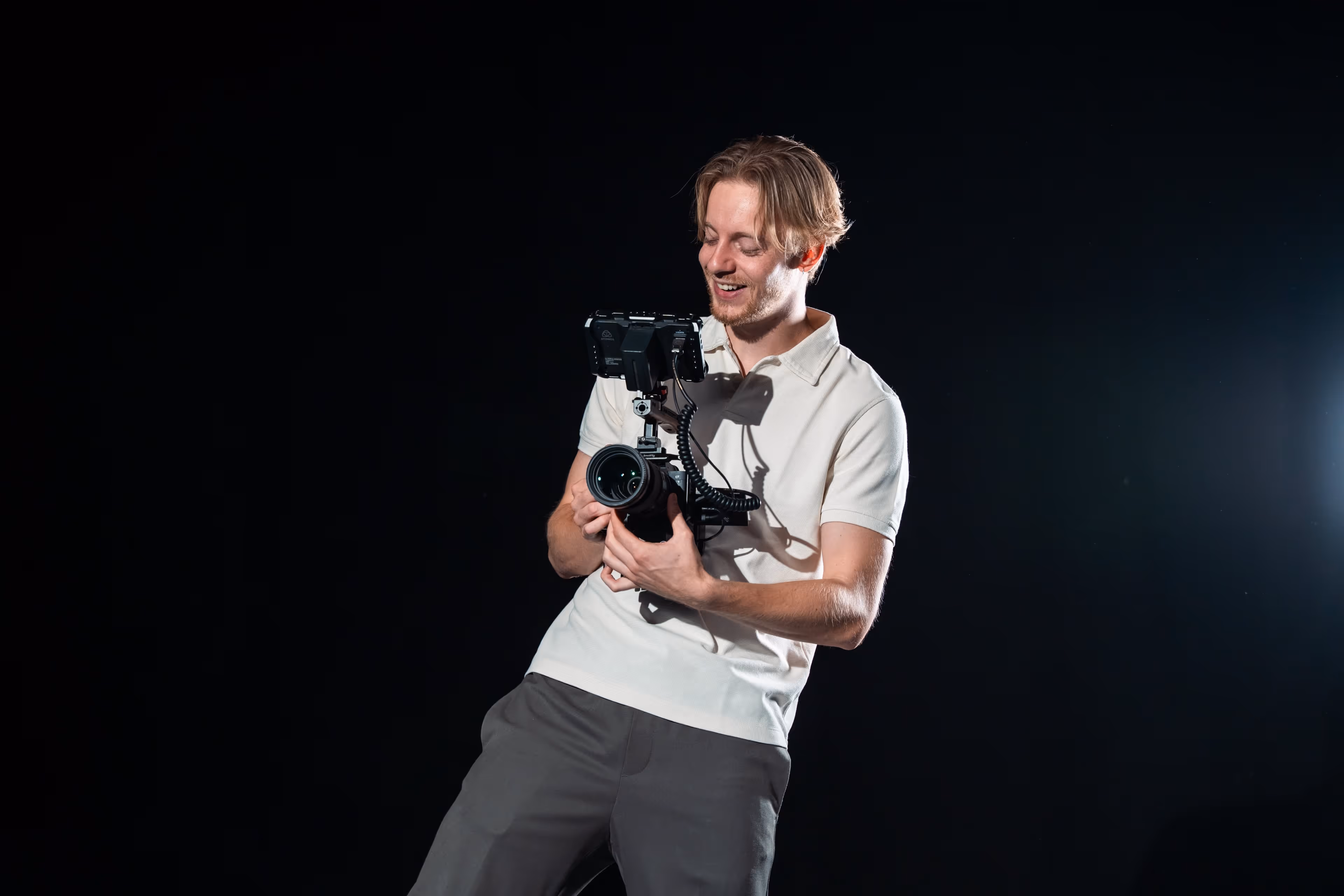 Jonge man met een licht overhemd die een professionele videocamera vasthoudt tegen een zwarte achtergrond.