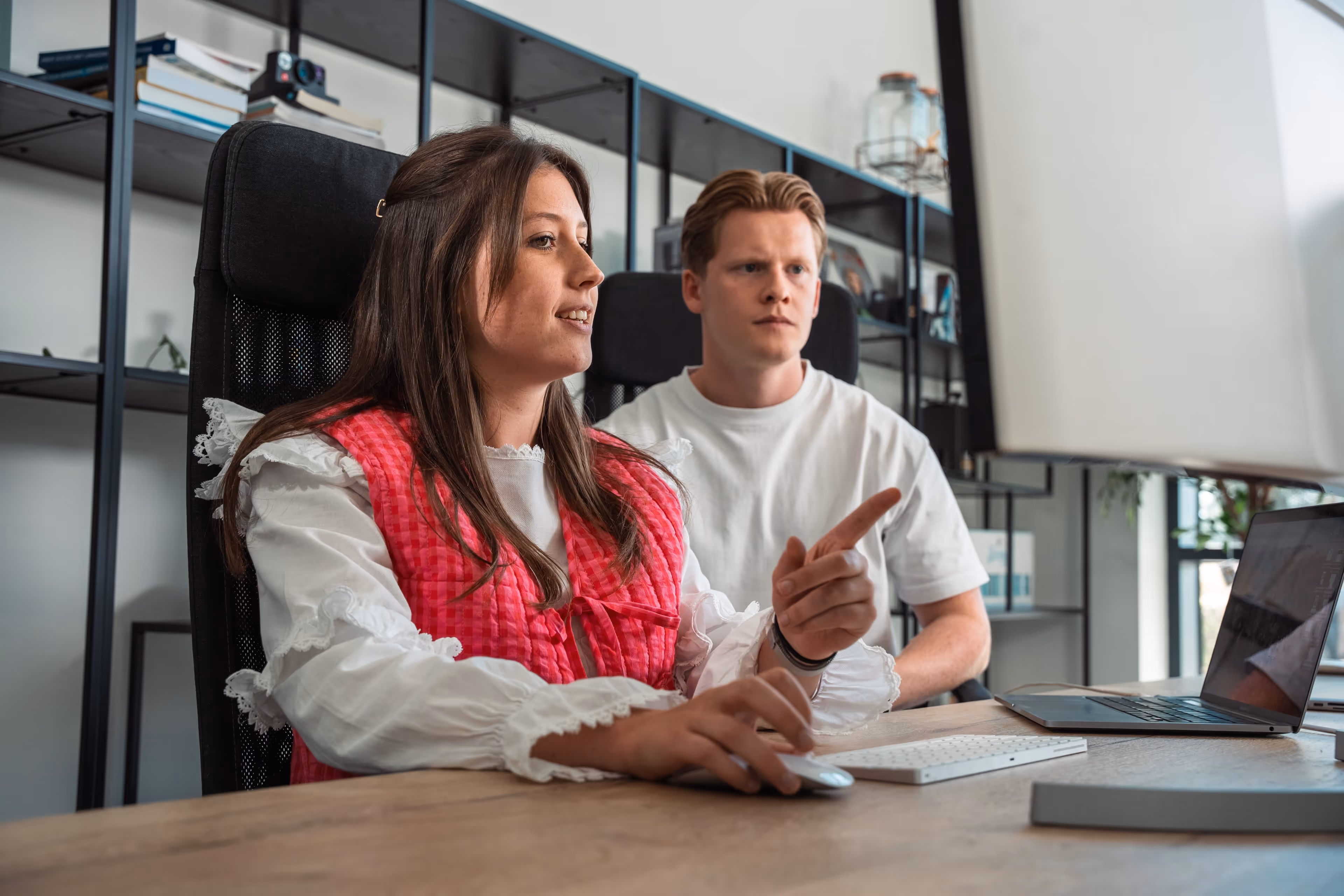 Twee jonge professionals werken samen aan een computer in een modern kantoor.