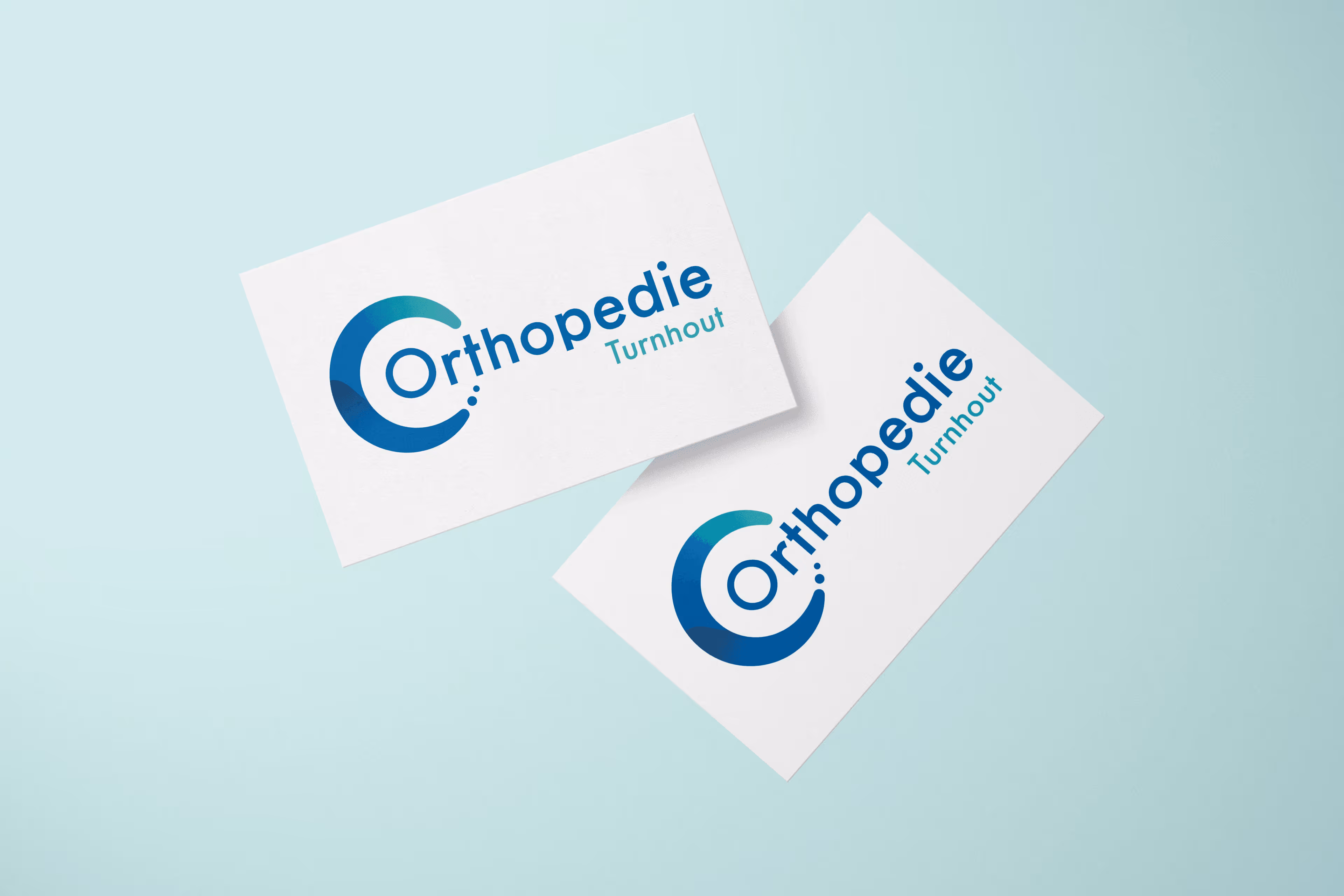 Twee witte visitekaartjes met het logo en de tekst 'Orthopedie Turnhout' op een lichtblauwe achtergrond.