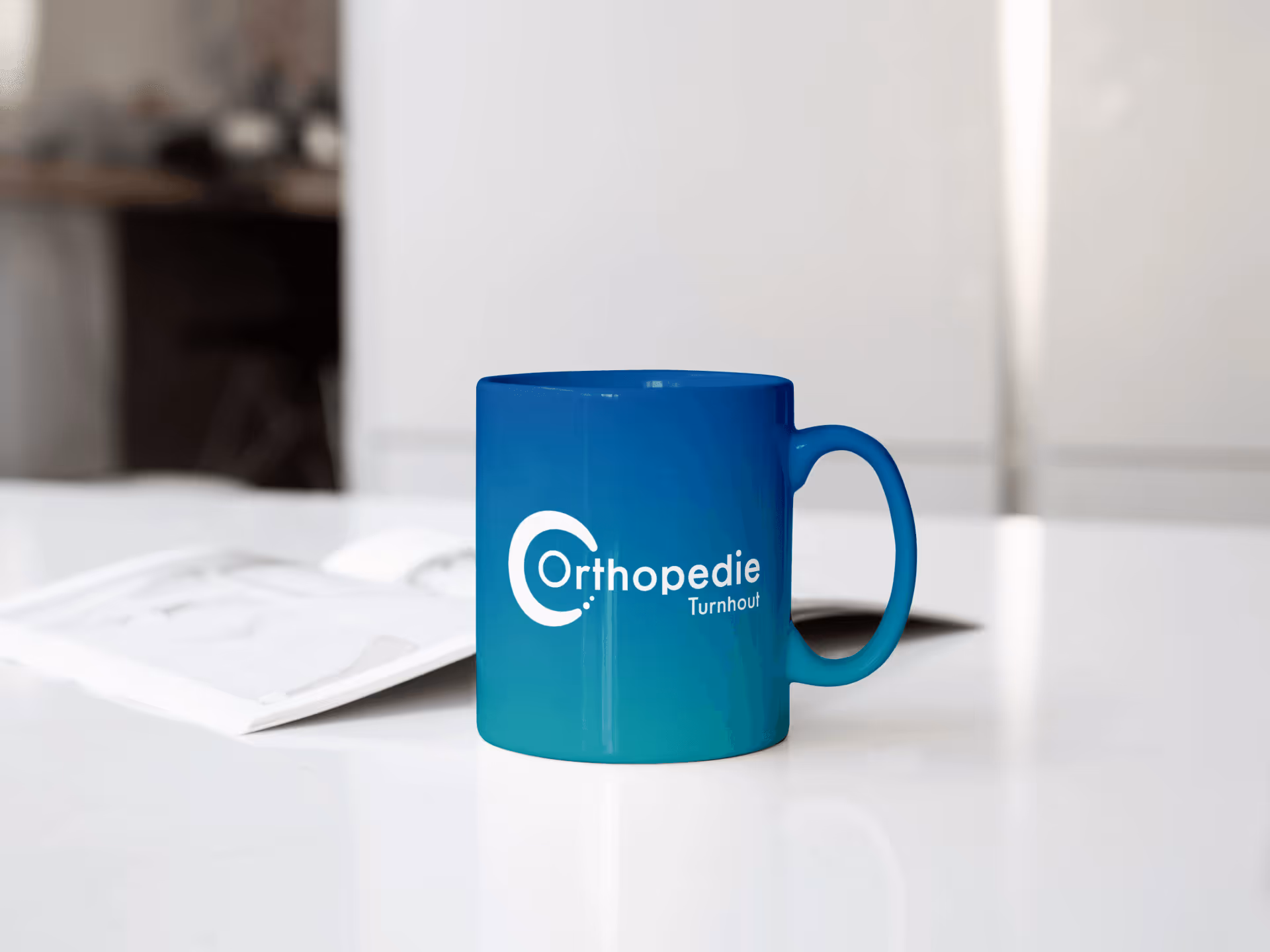 Blauwe mok met logo Orthopedie Turnhout op een witte tafel met tijdschrift op de achtergrond.