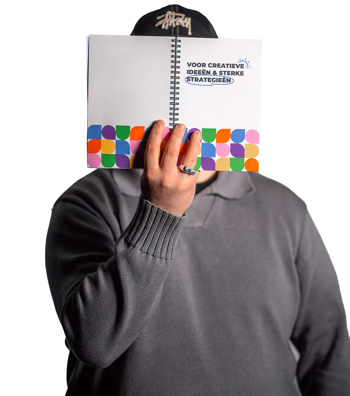 Persoon in grijze trui en zwarte pet houdt een open notitieboekje vast met de tekst 'Voor creatieve ideeën & sterke strategieën' en kleurrijk patroon onderaan.
