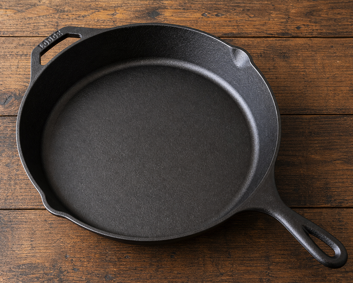 A black cast iron skillet rests on a rustic wooden surface, showing textured interior, wide cooking area, sturdy handle, and durable kitchen design.