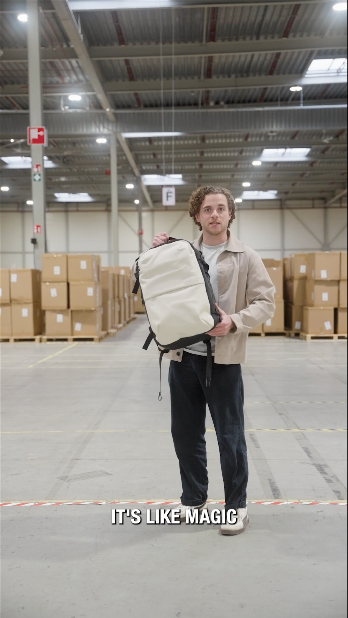 A young man standing in a warehouse holding a backpack