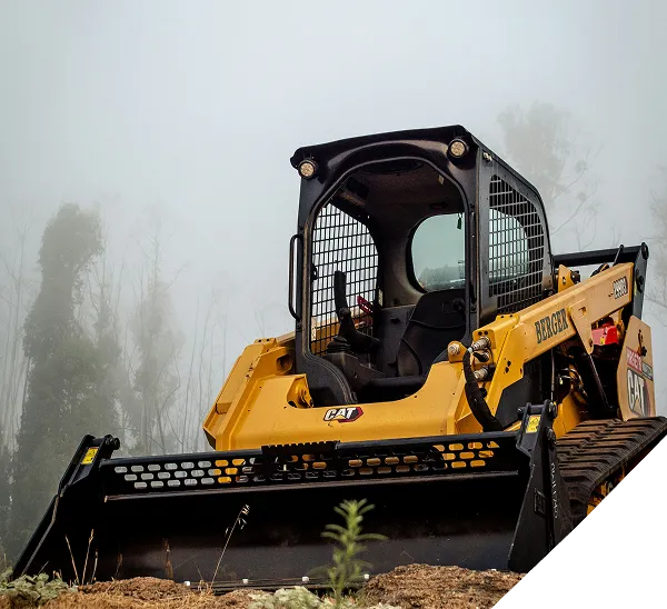 A yellow Caterpillar skid steer loader with a front bucket attachment sits on dirt, surrounded by fog and tall, faintly visible trees in the background.