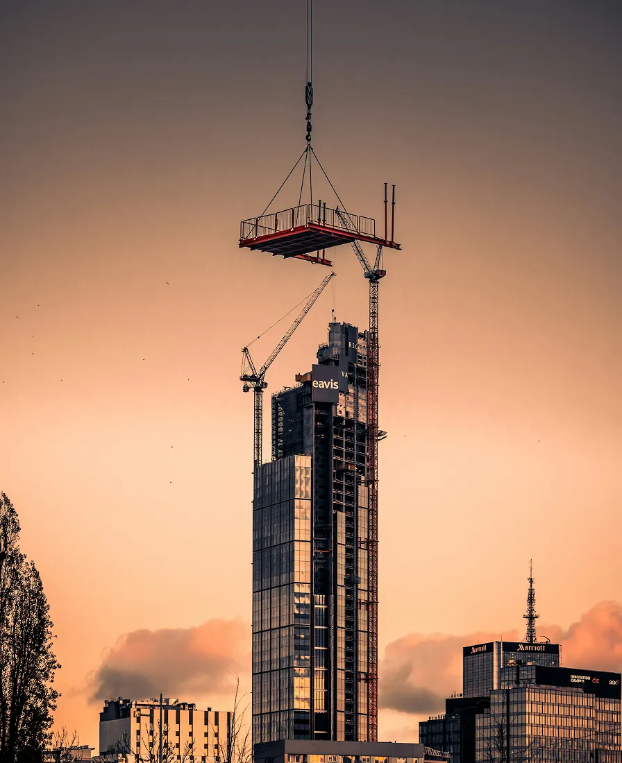 Tall Caavis building under construction with cranes at sunset