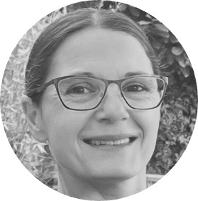 Smiling woman wearing glasses with a natural background of leaves.