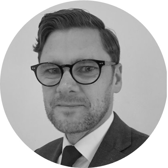 Black and white portrait of a man with short hair, wearing round glasses, a suit, white shirt, and dark tie.