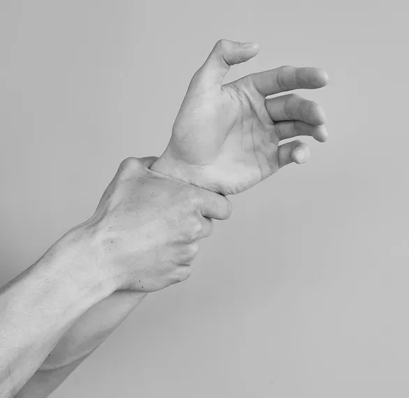 Zdjęcie dłoni mocno ściskającej nadgarstek na szarym tle, symbolizujące napięcie, stres lub ból fizyczny w kontekście terapii psychologicznej w Centrum Terapii i Rozwoju.