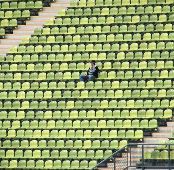 Zdjęcie samotnej osoby siedzącej na pustych zielonych trybunach stadionu, symbolizujące izolację lub samotność w kontekście terapii psychologicznej w Centrum Terapii i Rozwoju.