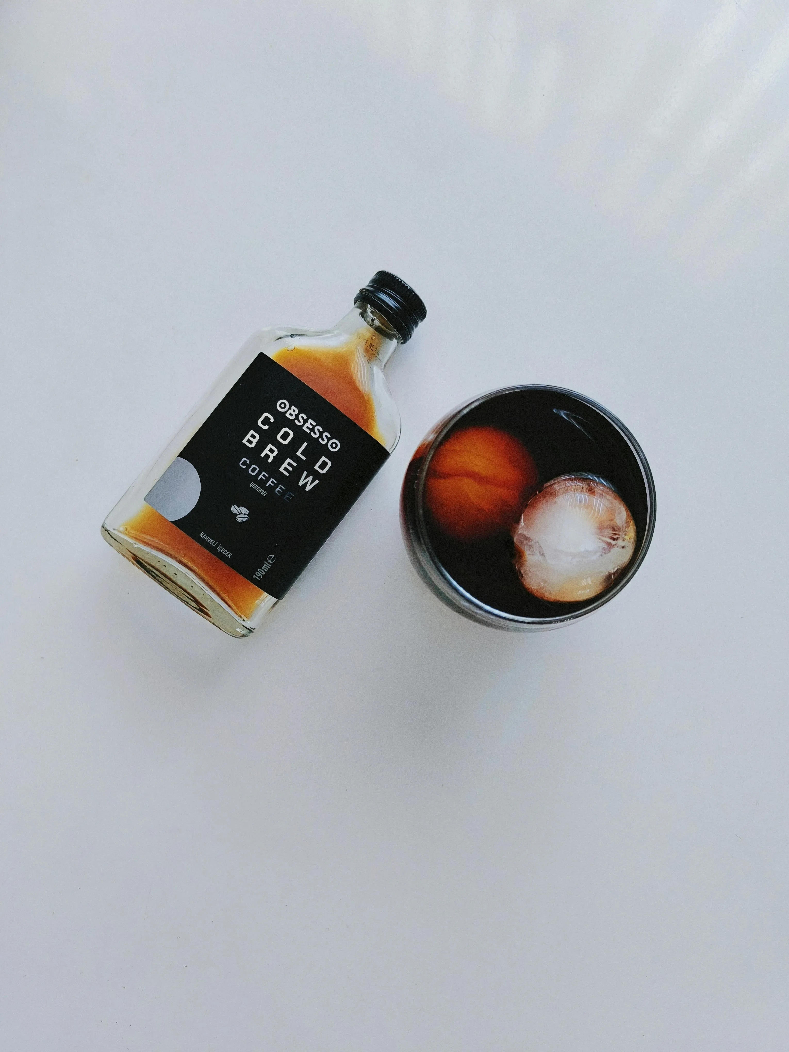 Butelka cold brew coffee "OBSESSO" obok szklanki z lodem i kawą, symbolizująca uzależnienie od kofeiny lub nawyki w terapii w Centrum Terapii i Rozwoju.
