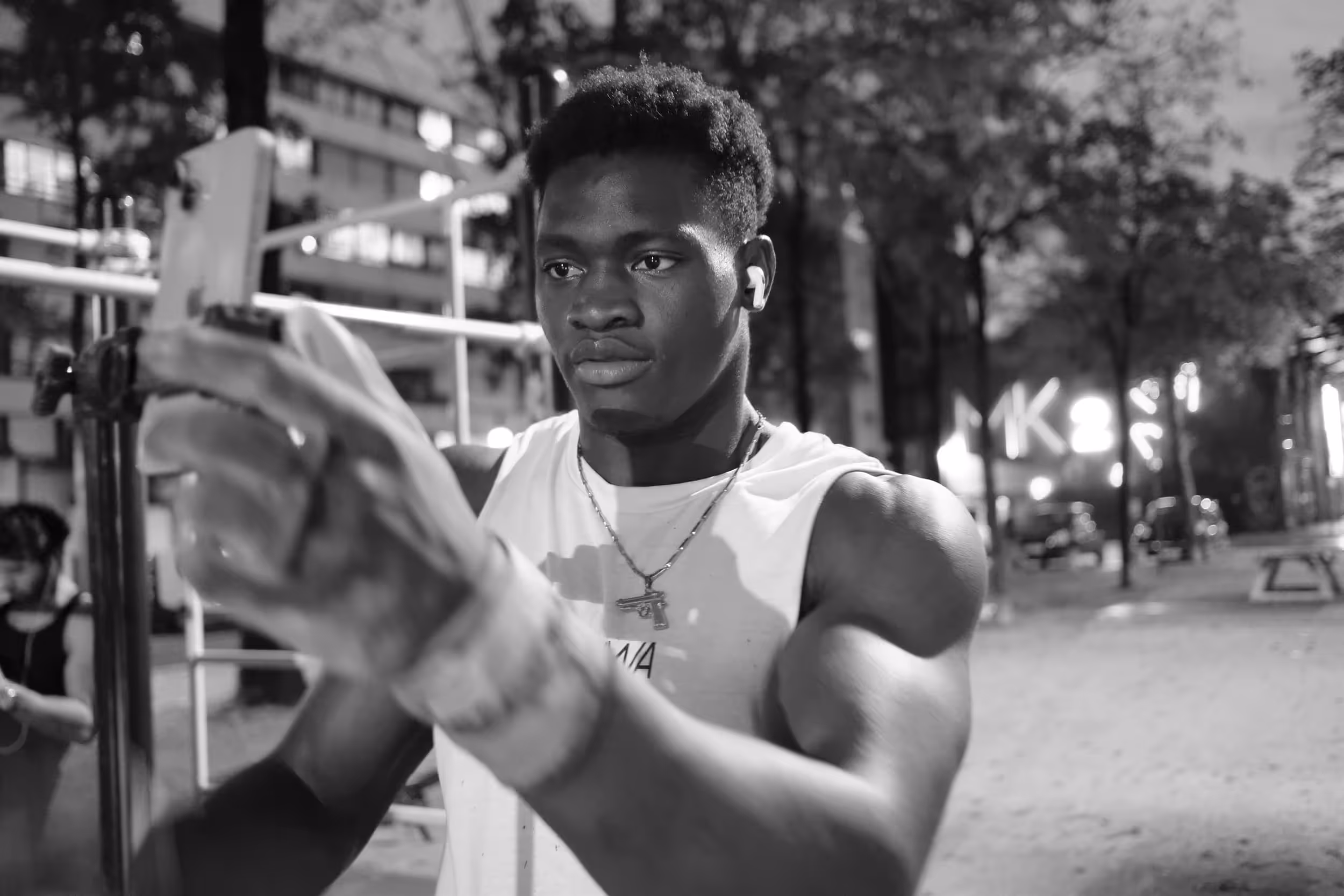 Homme musclé tenant un smartphone, probablement en train de se prendre en selfie, en extérieur de nuit.