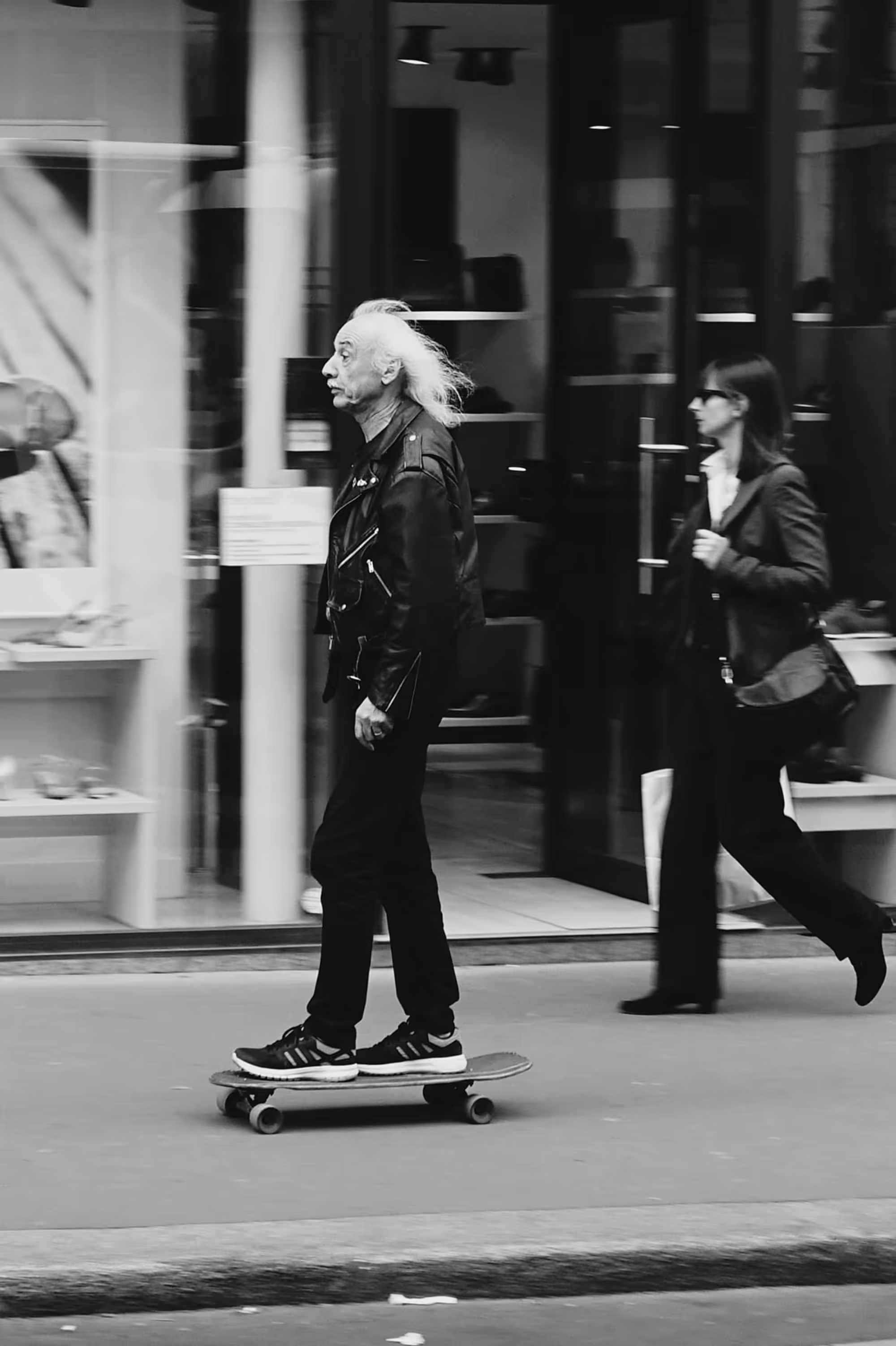 Homme âgé aux cheveux longs et blancs faisant du skateboard en centre-ville.