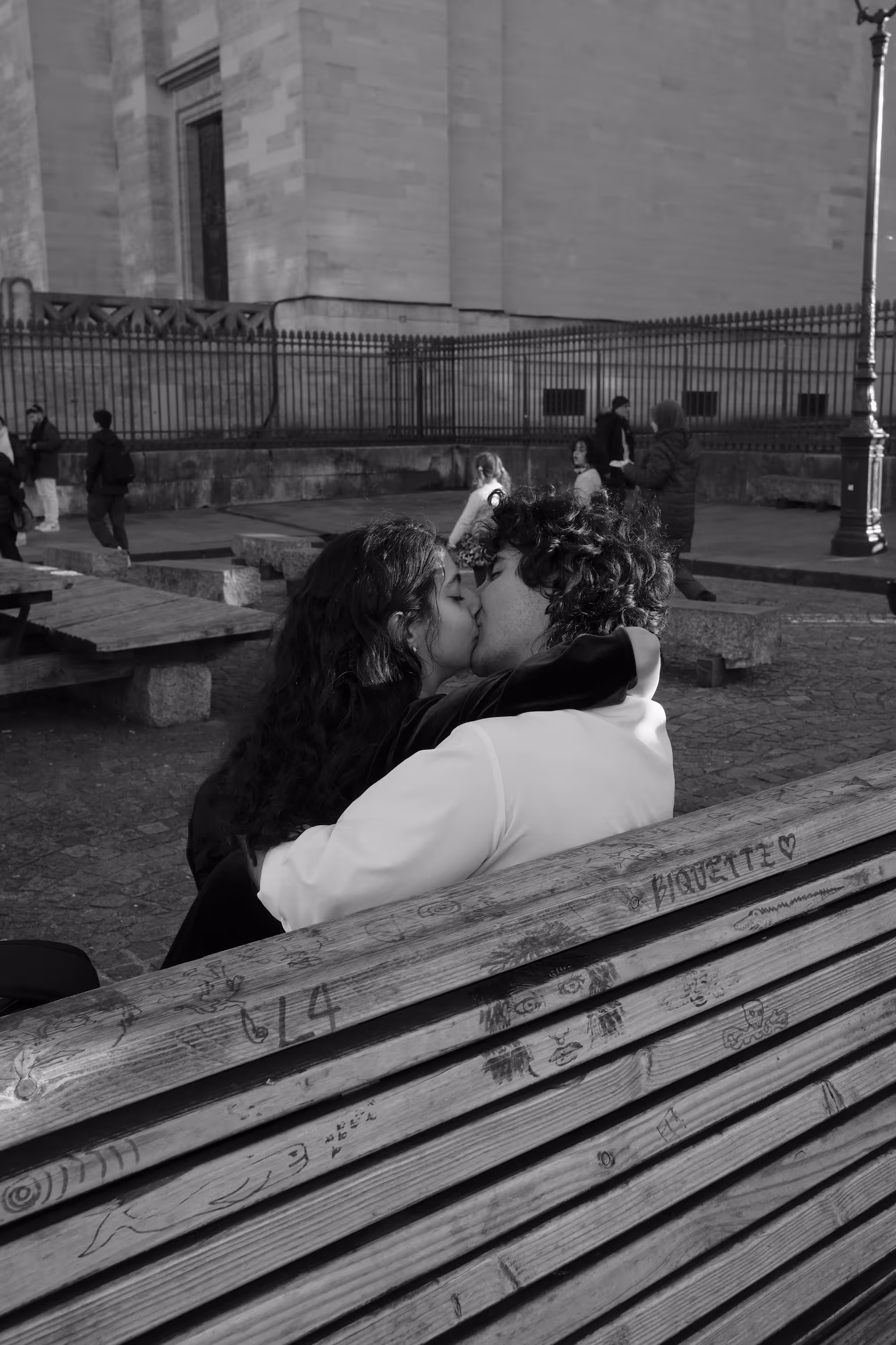 Jeune couple s’embrassant tendrement sur un banc en bois gravé.
