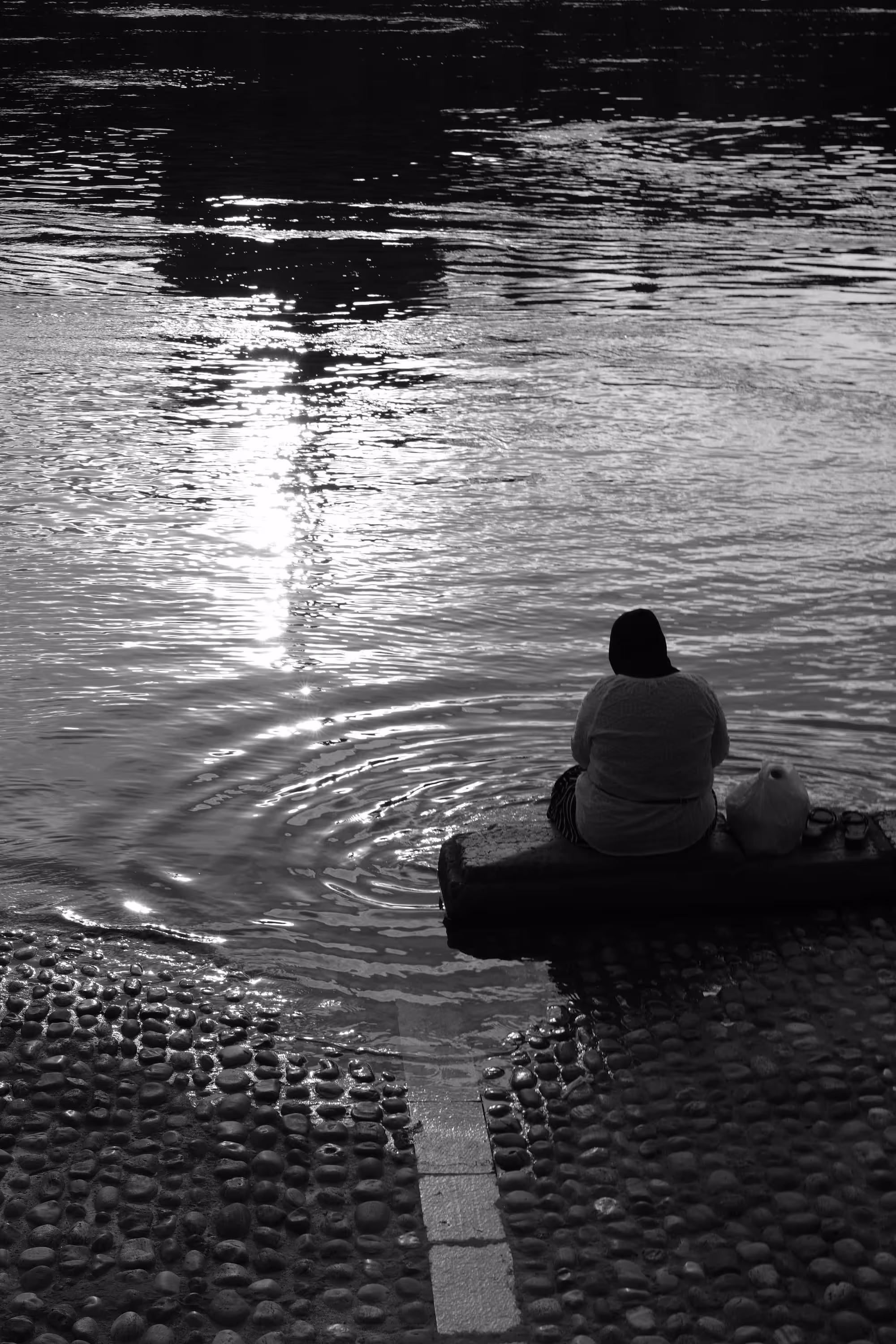 Femme assise au bord d’un fleuve, regardant le reflet du soleil sur l’eau.