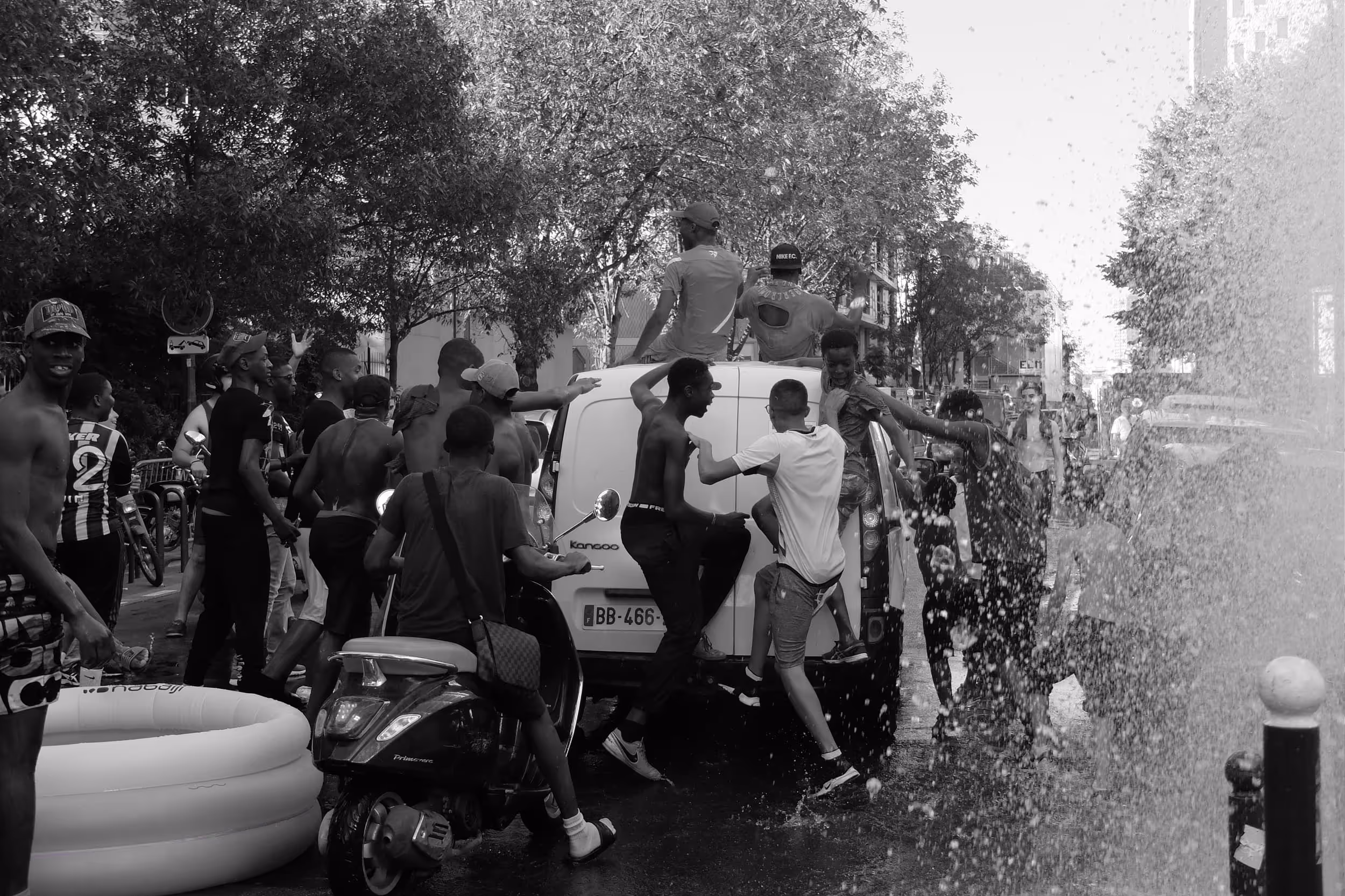 Groupe de jeunes autour d’un van sous un jet d’eau en pleine rue, ambiance estivale et festive.