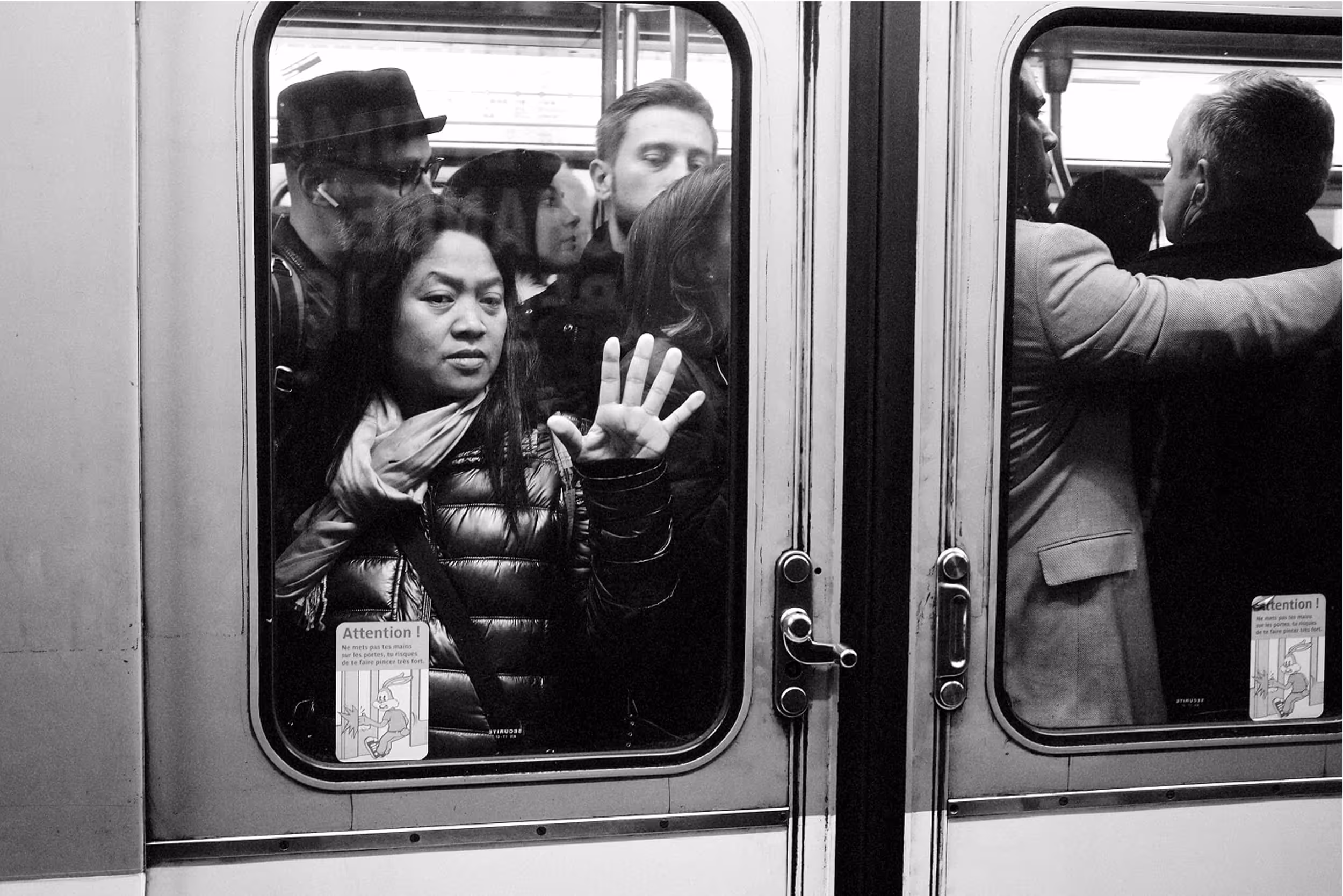 Scène de foule serrée contre la vitre d'une rame de métro, plusieurs visages tendus, ambiance étouffante.