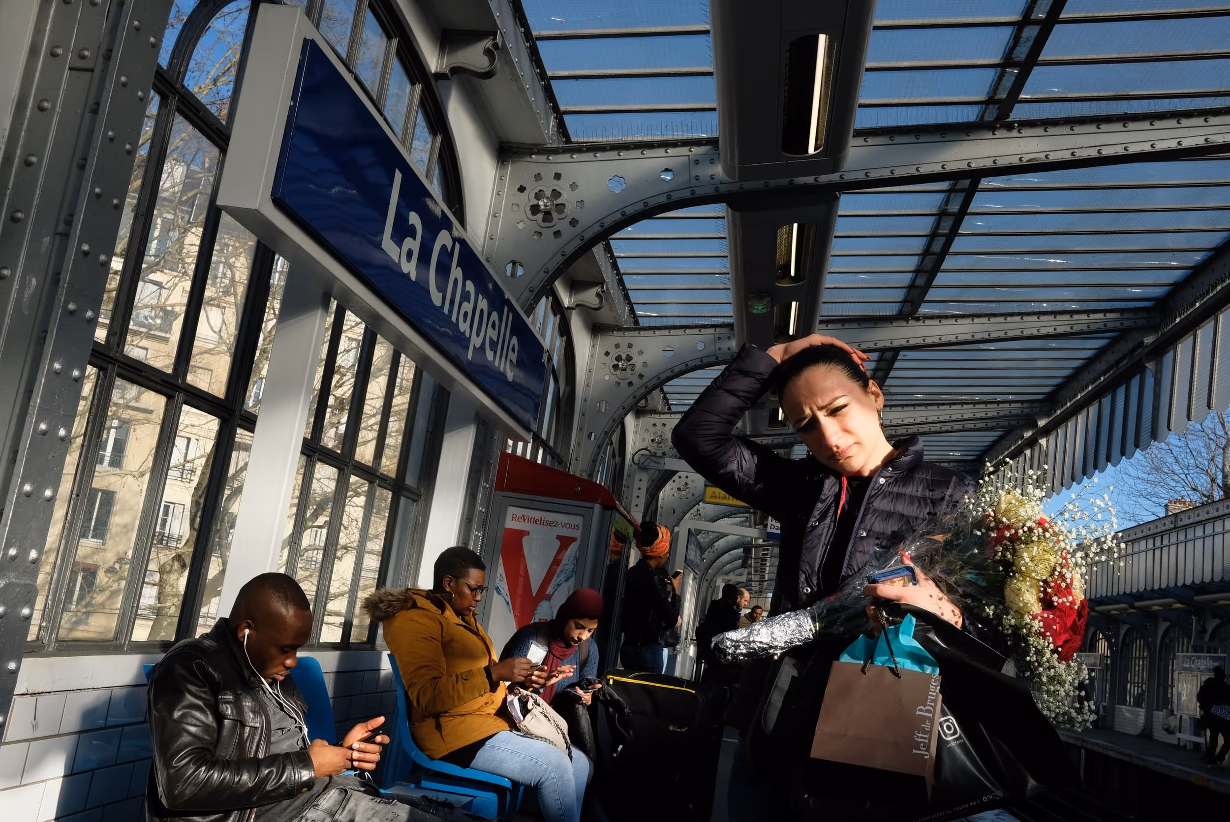 Groupe de personnes assises et debout sur le quai de la station La Chapelle, en pleine lumière naturelle.