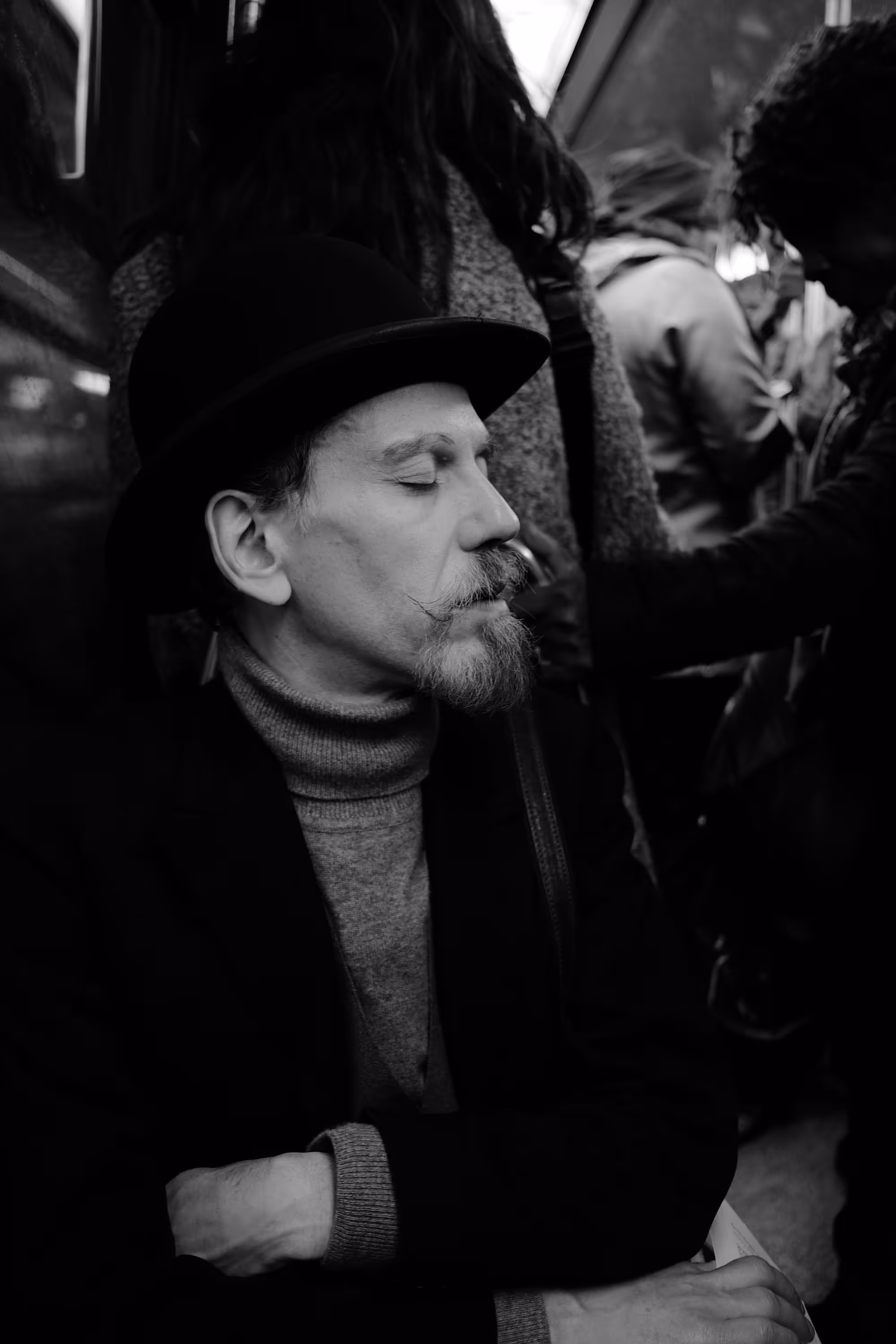 Un homme avec un chapeau melon et une moustache, endormi dans une rame de métro bondée.