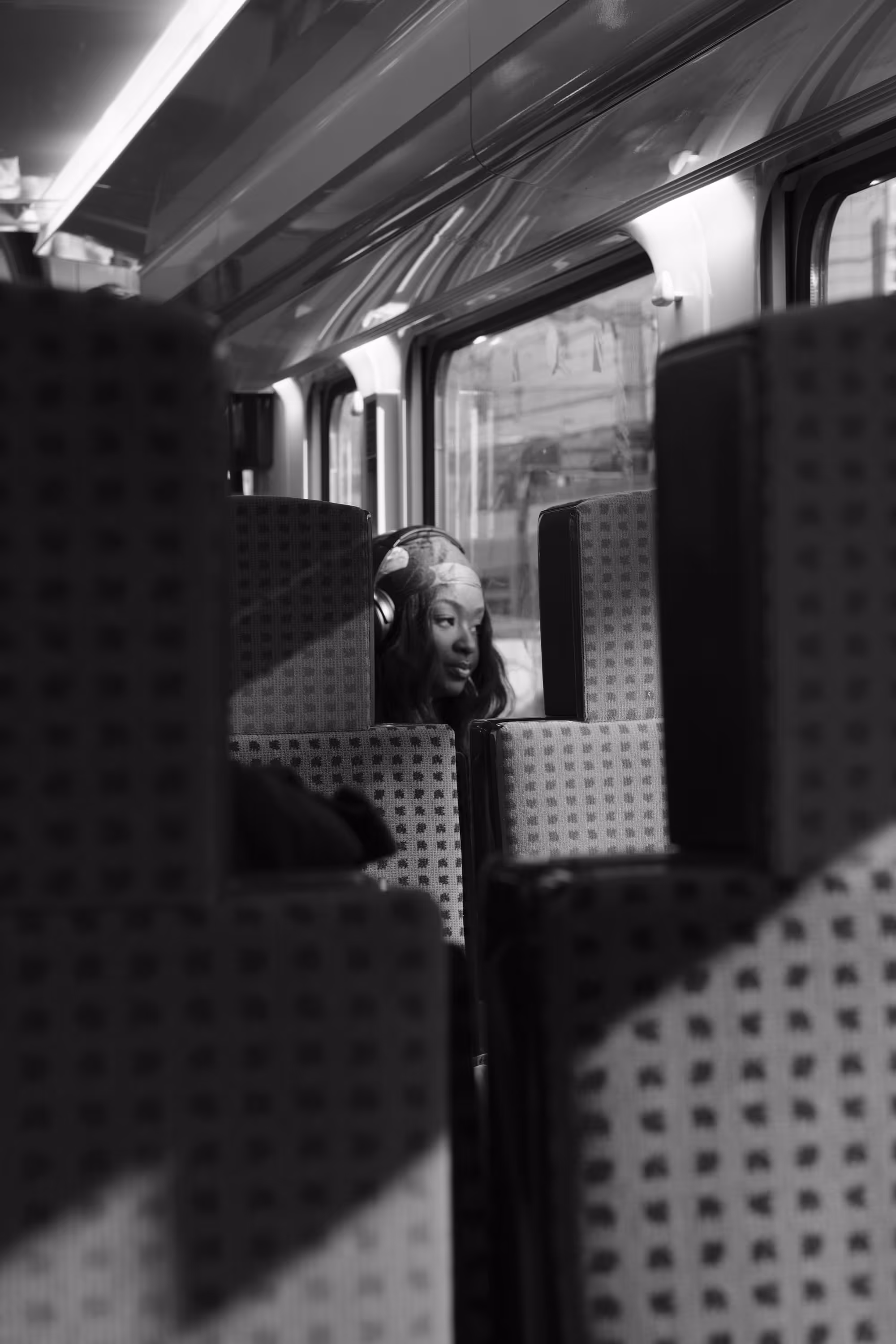 Une femme noire portant un casque audio regarde au loin, assise dans un train entre deux rangées de sièges.