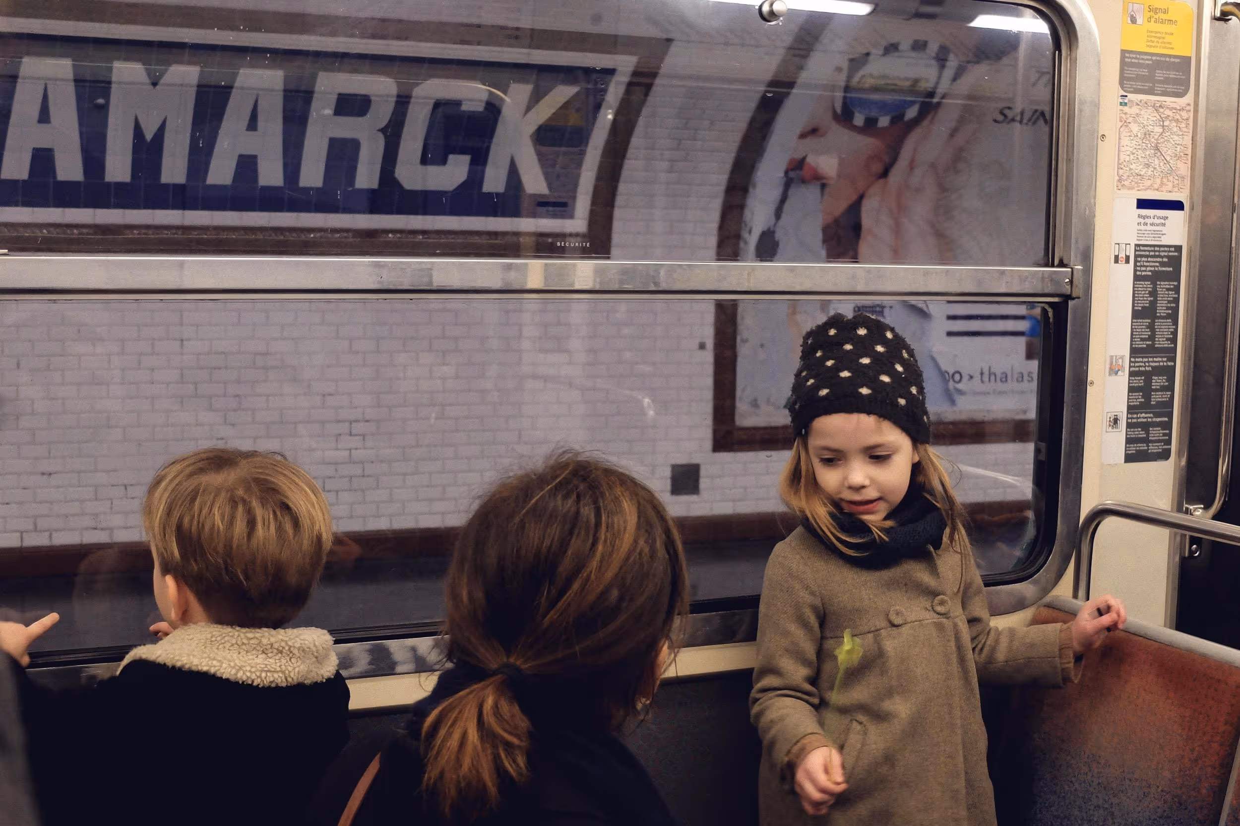Deux jeunes enfants et une femme regardant à travers la vitre du métro en station.