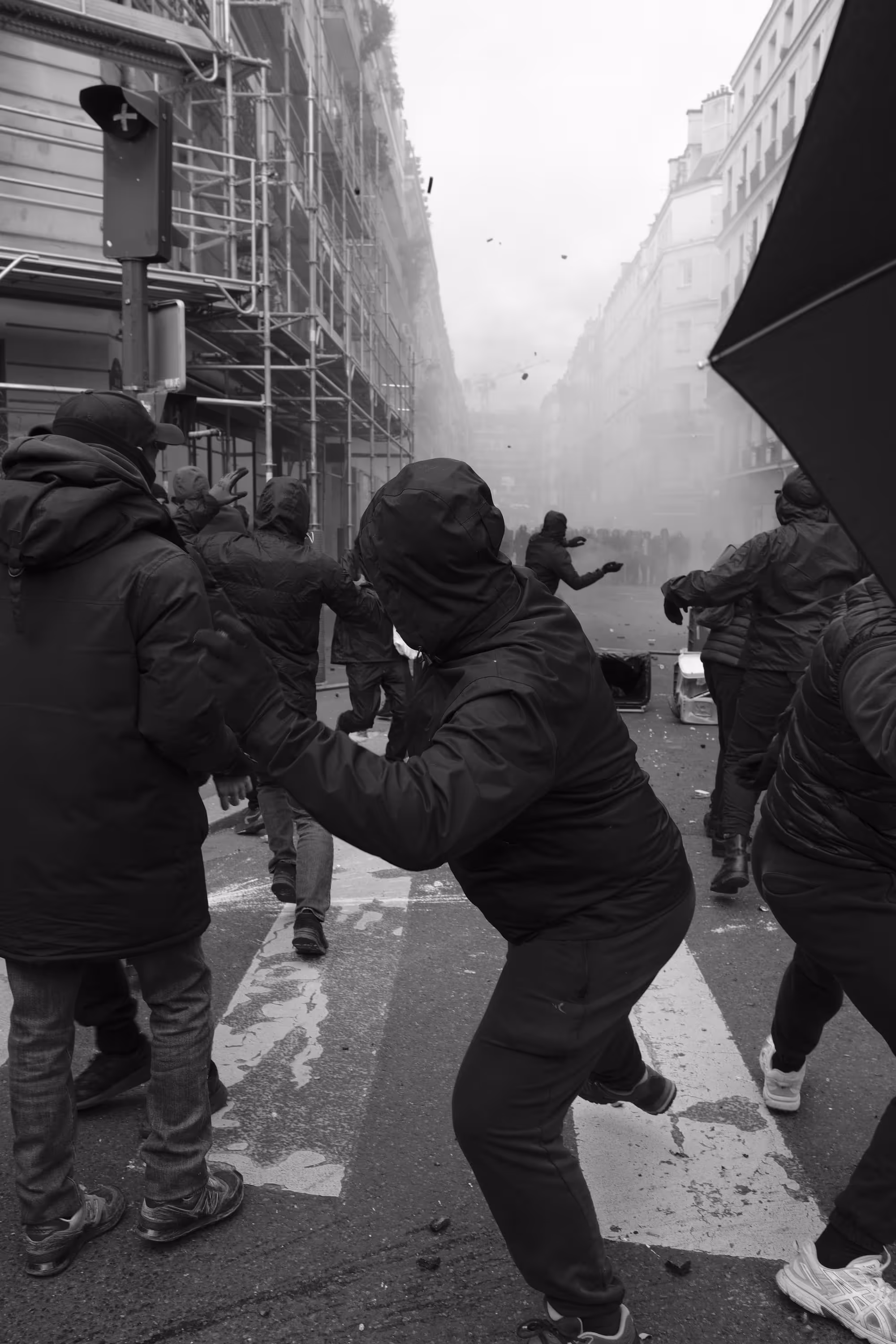Personnes encapuchonnées lançant des projectiles dans une rue remplie de fumée.