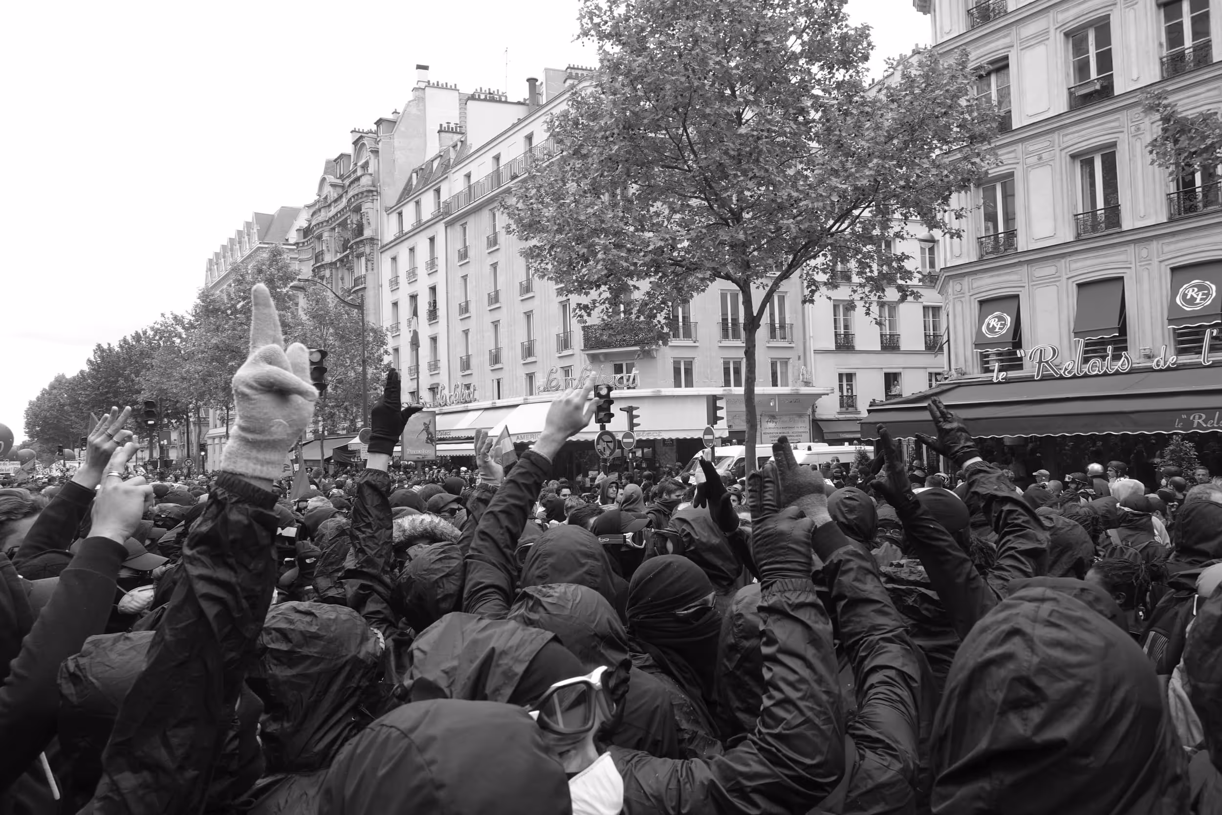 Foule dense de manifestants vêtus de noir levant le poing dans une rue parisienne bordée d'immeubles haussmanniens.