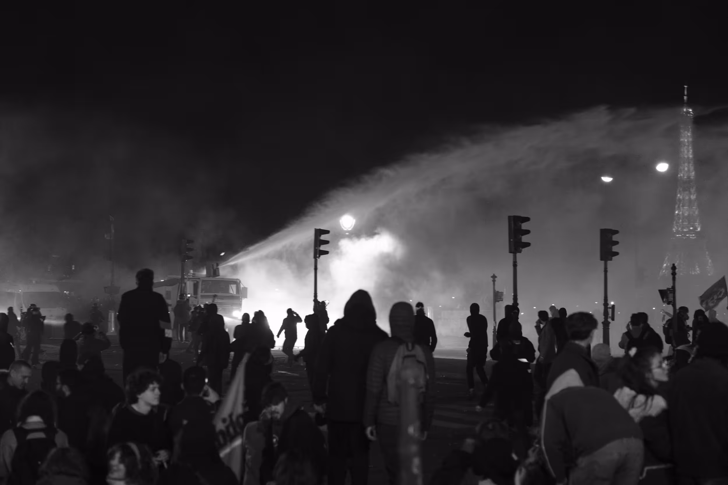 Manifestation nocturne à Paris avec canon à eau et la tour Eiffel visible en arrière-plan.