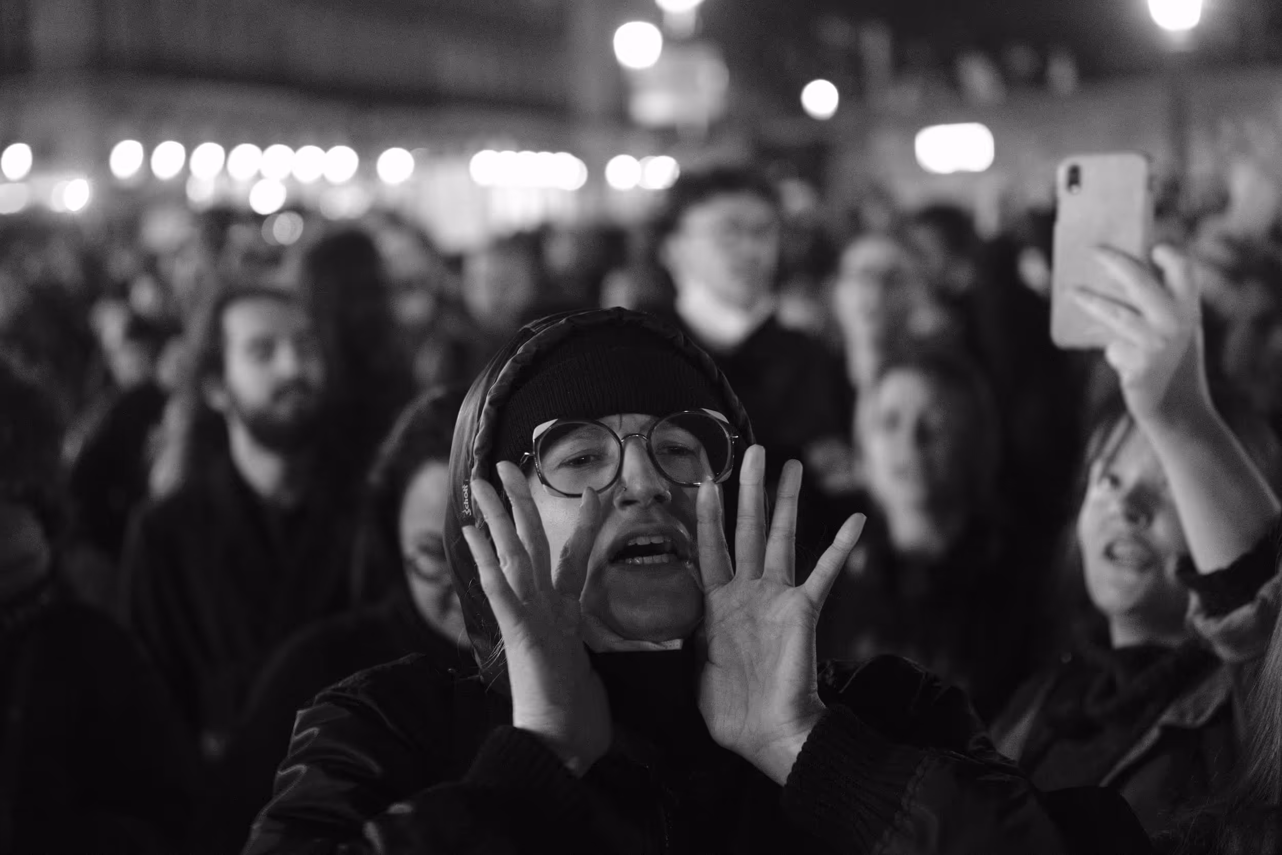 Manifestant criant en pleine nuit, entouré d’une foule où une femme filme avec son smartphone.