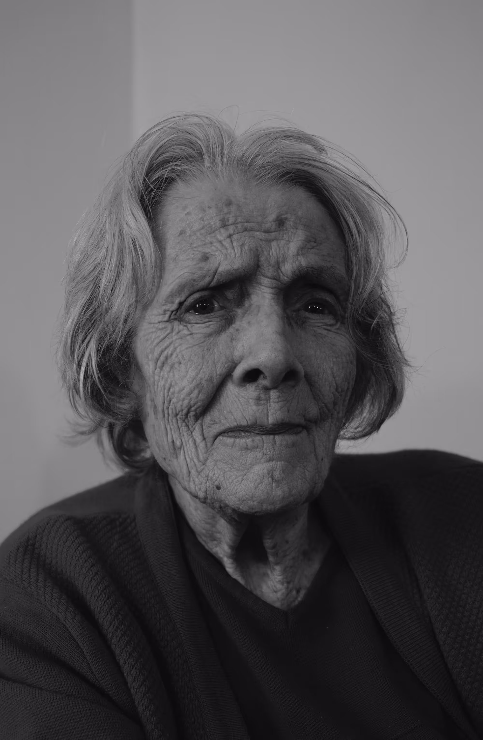 Portrait en noir et blanc d'une femme âgée, regardant l'objectif avec intensité, les traits marqués par le temps.