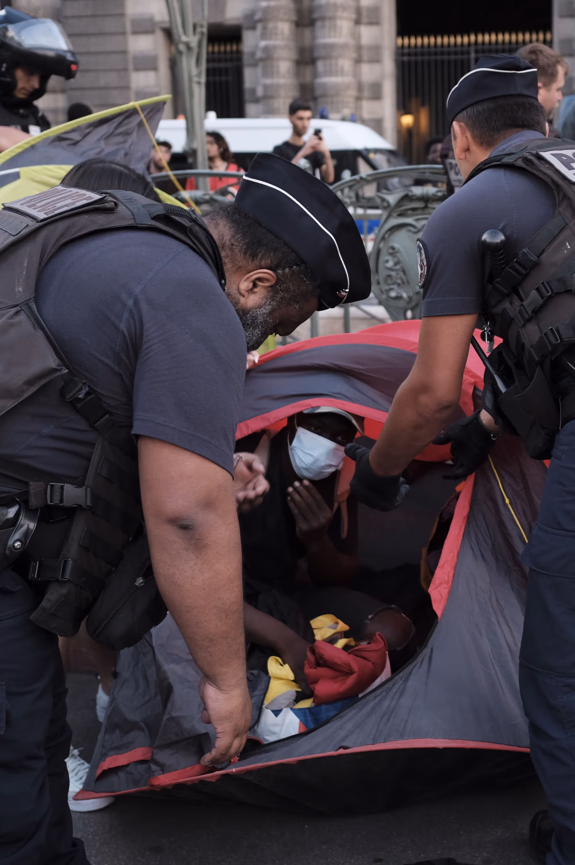 Deux policiers penchés au-dessus d’une tente rouge, regardant à l’intérieur.