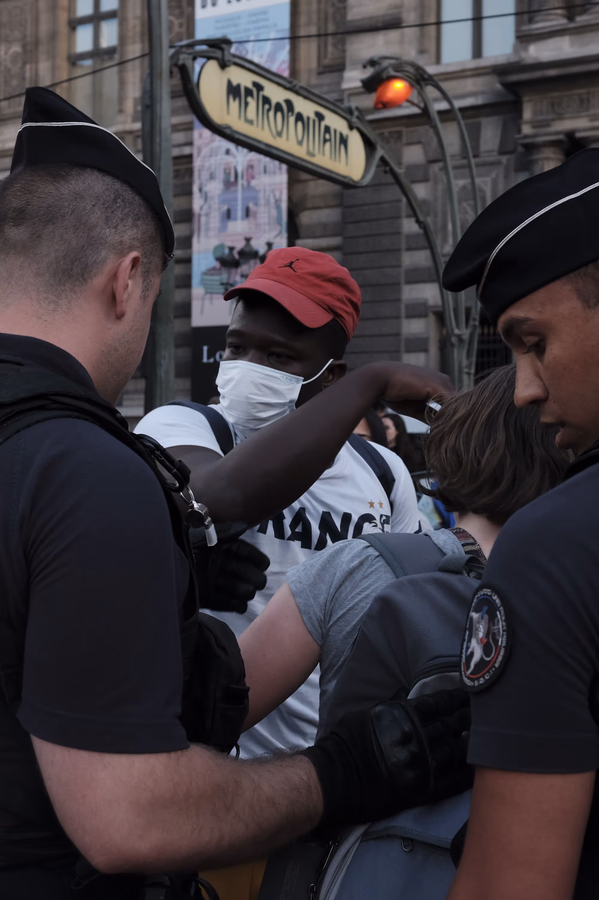 Un homme masqué discutant avec des policiers devant une bouche de métro.
