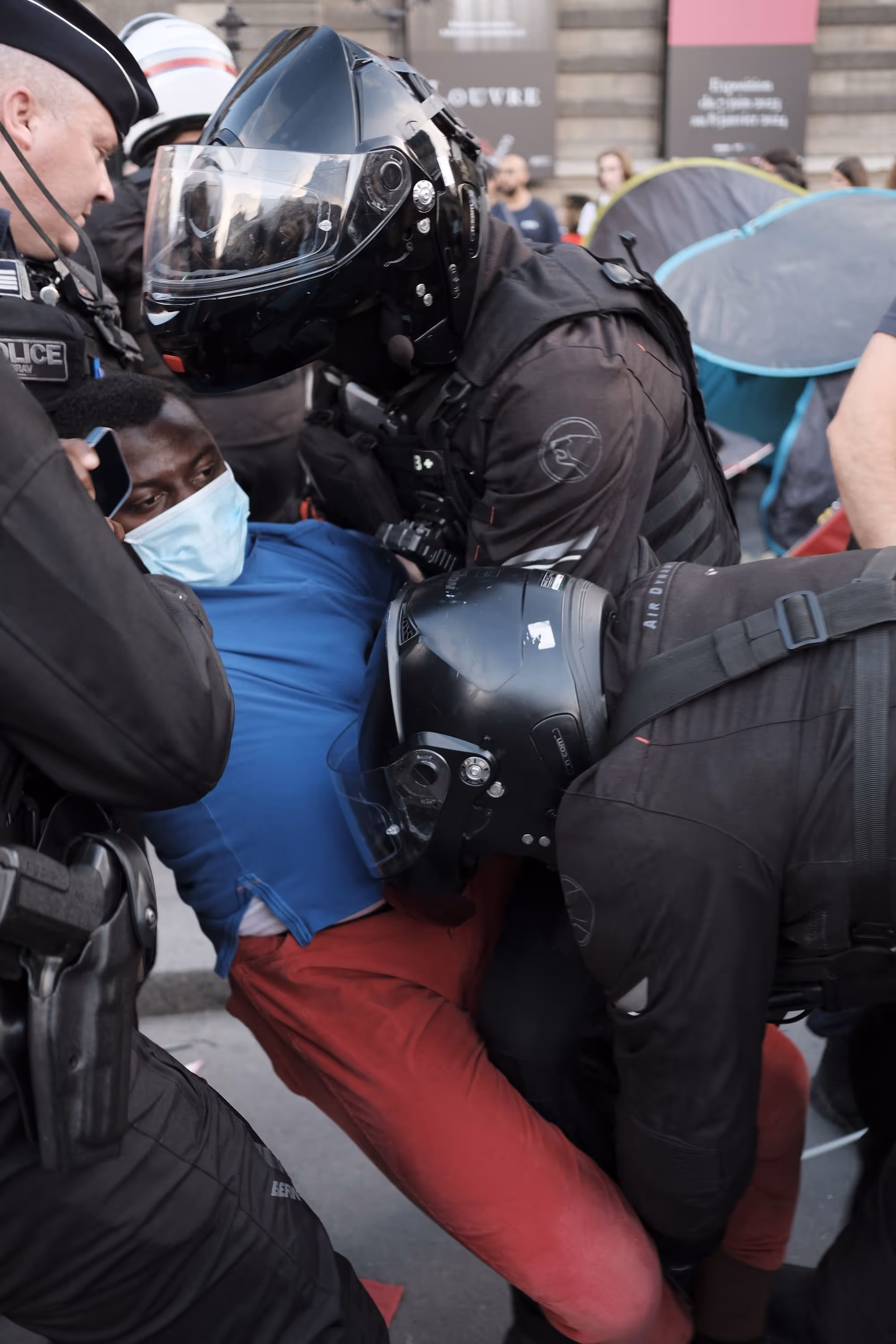 Homme au sol, masqué, encerclé par des policiers casqués.