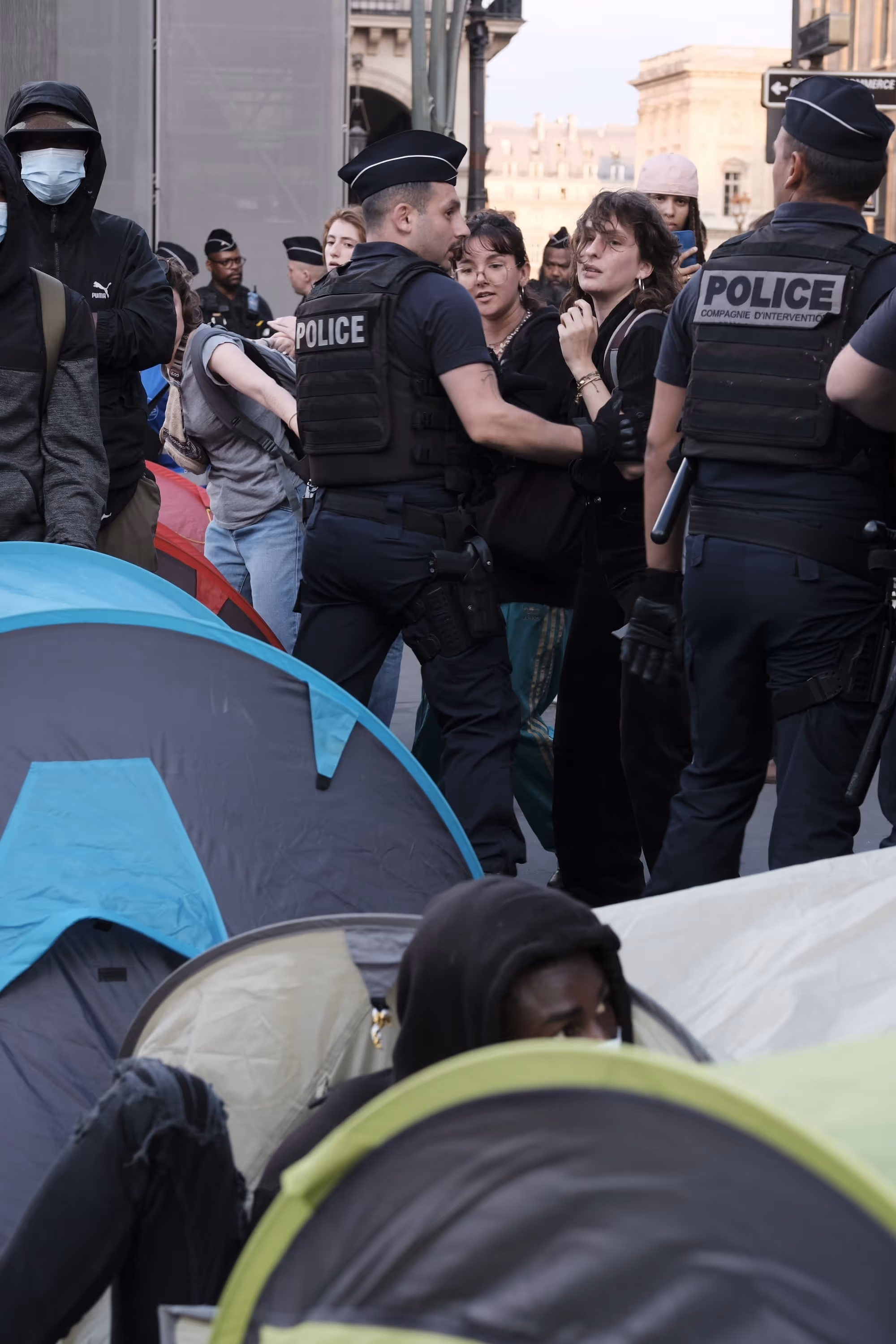 Femmes interpellées par la police au milieu de tentes de manifestants.