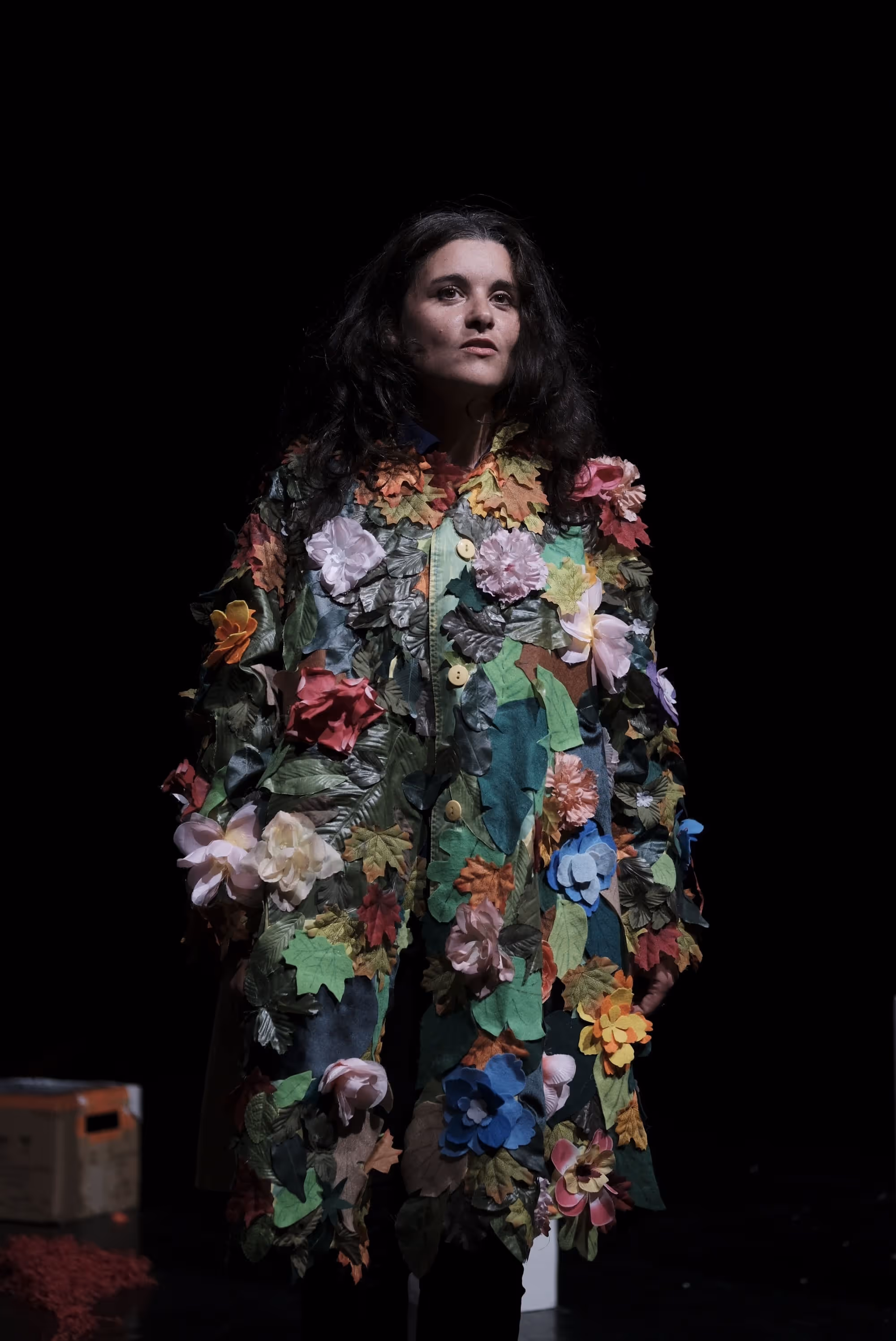 Femme portant une veste décorée de fleurs en tissu, debout sur scène.