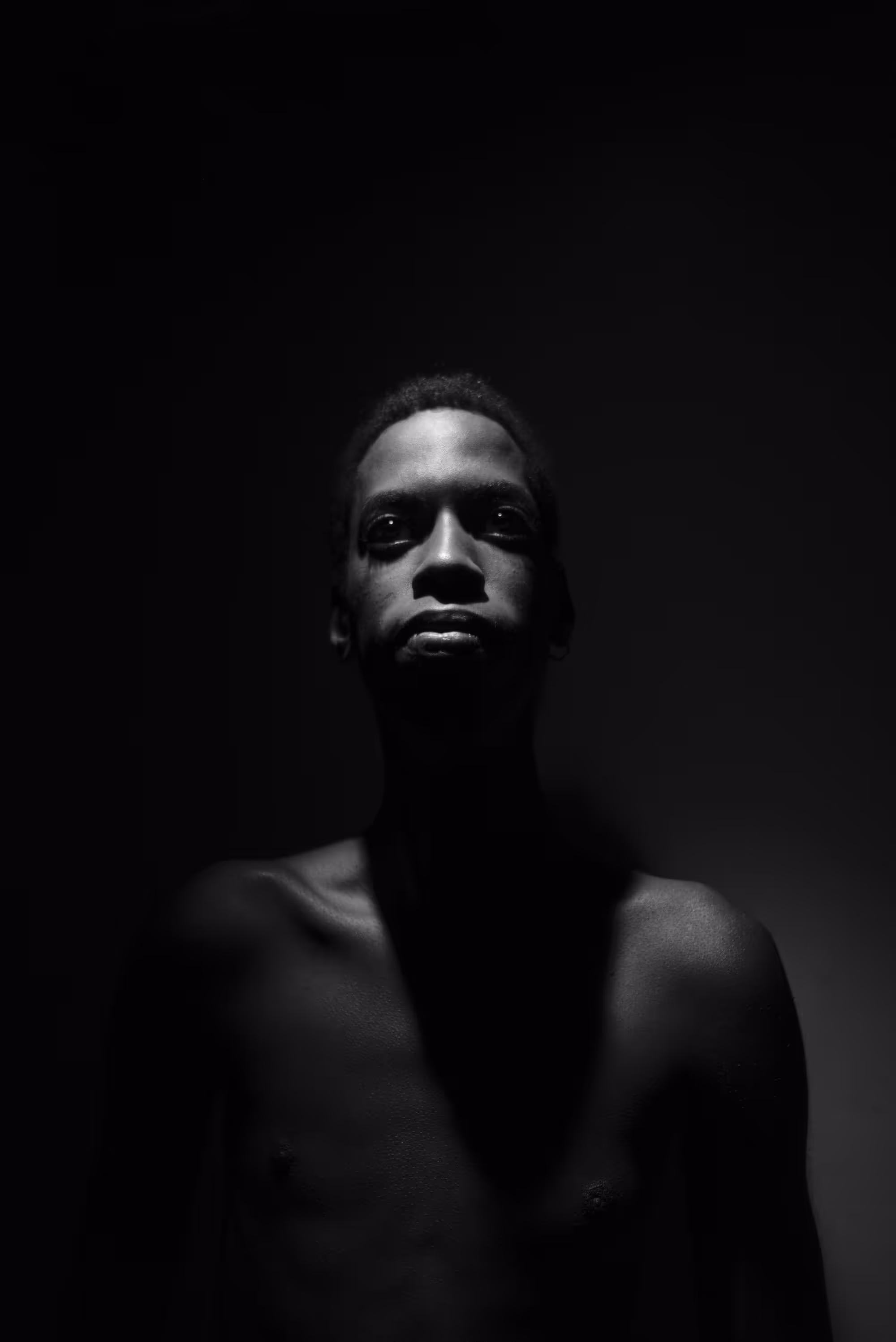 Portrait d’un homme torse nu dans une lumière dramatique, entouré d’ombres.