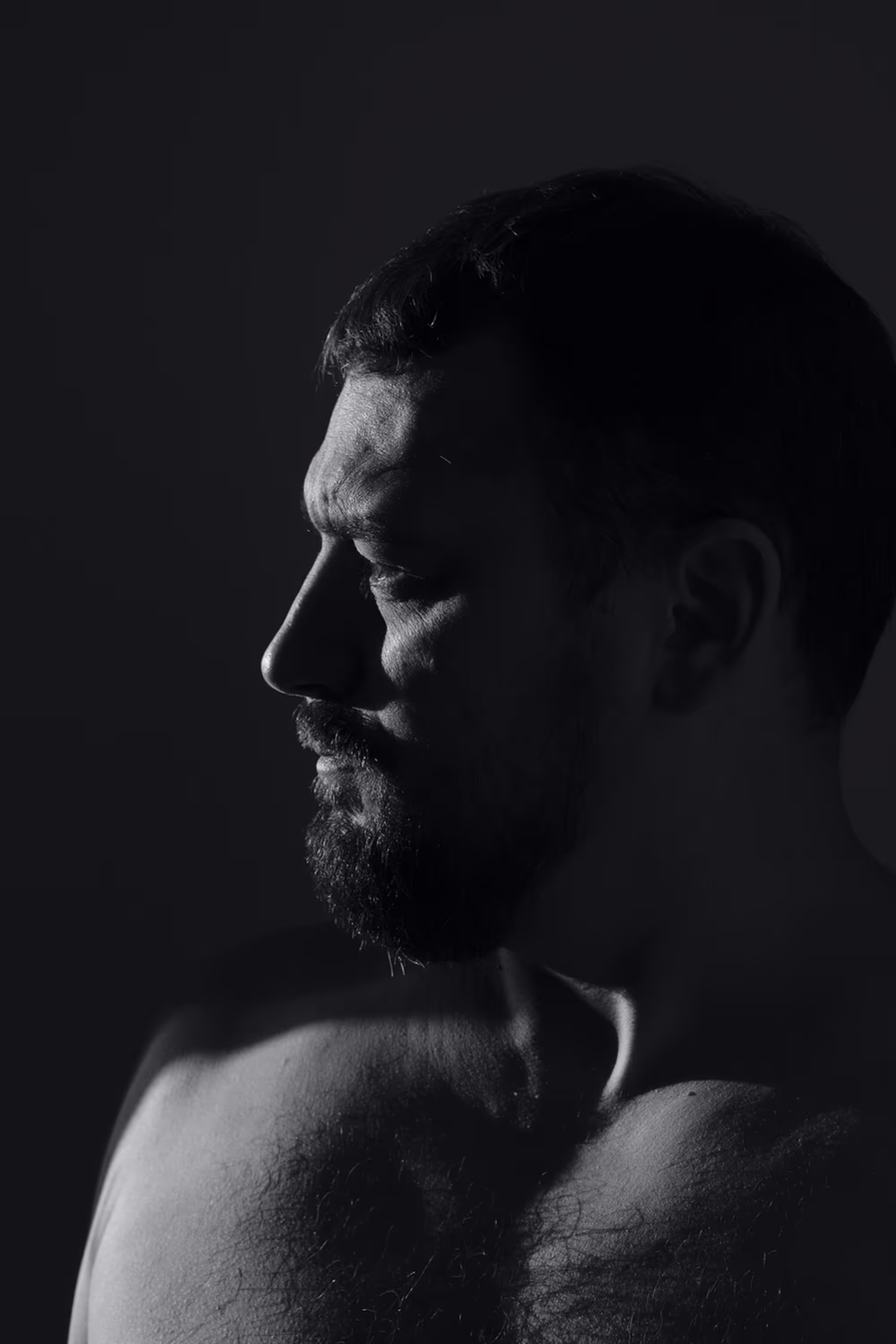 Portrait en clair-obscur d’un homme barbu de profil, regard tourné vers le sol.