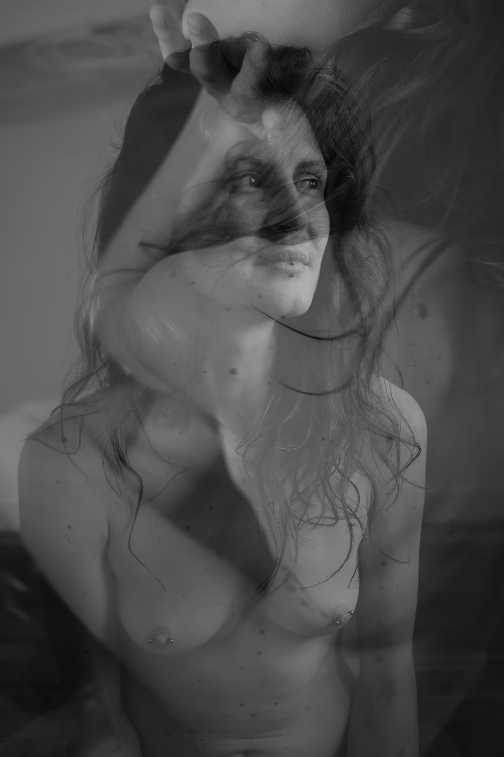 Double exposition d’une femme nue au regard franc, avec un bras et des cheveux superposés.