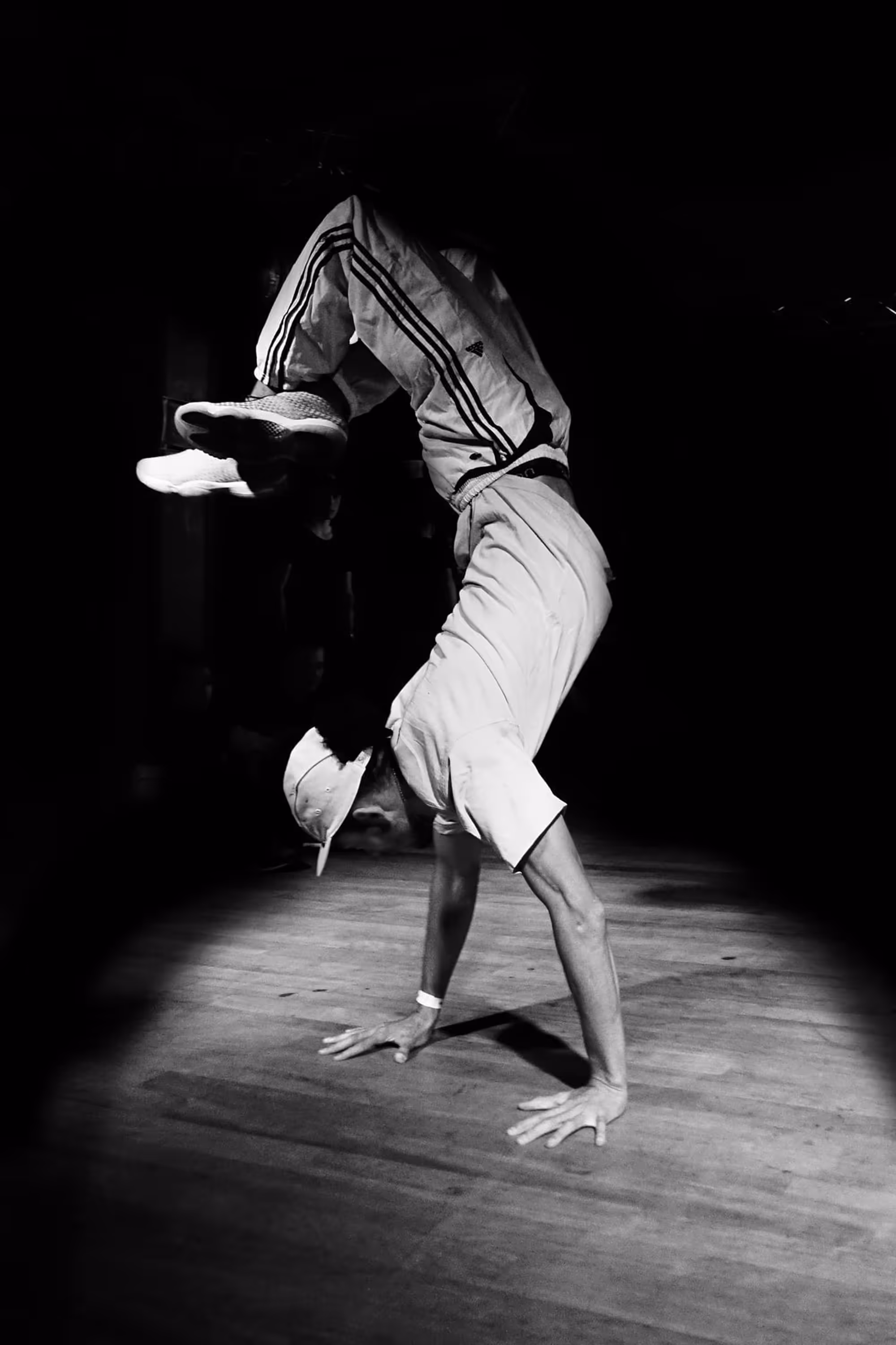 Danseur réalisant un poirier acrobatique en pleine lumière sur une scène sombre, capturé en mouvement suspendu.