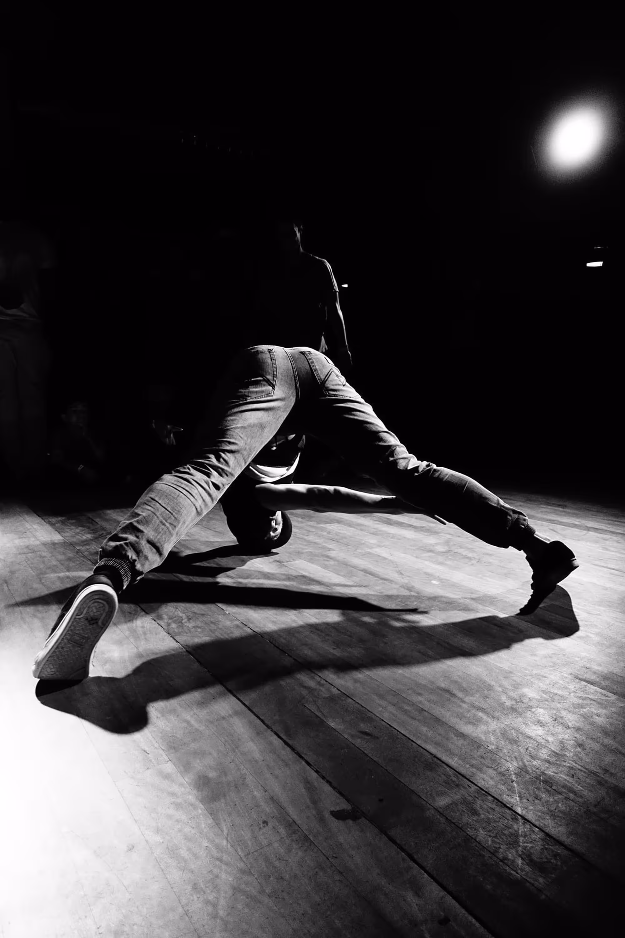 Danseur en position de pont arrière, les jambes tendues, ombre projetée sur le parquet.