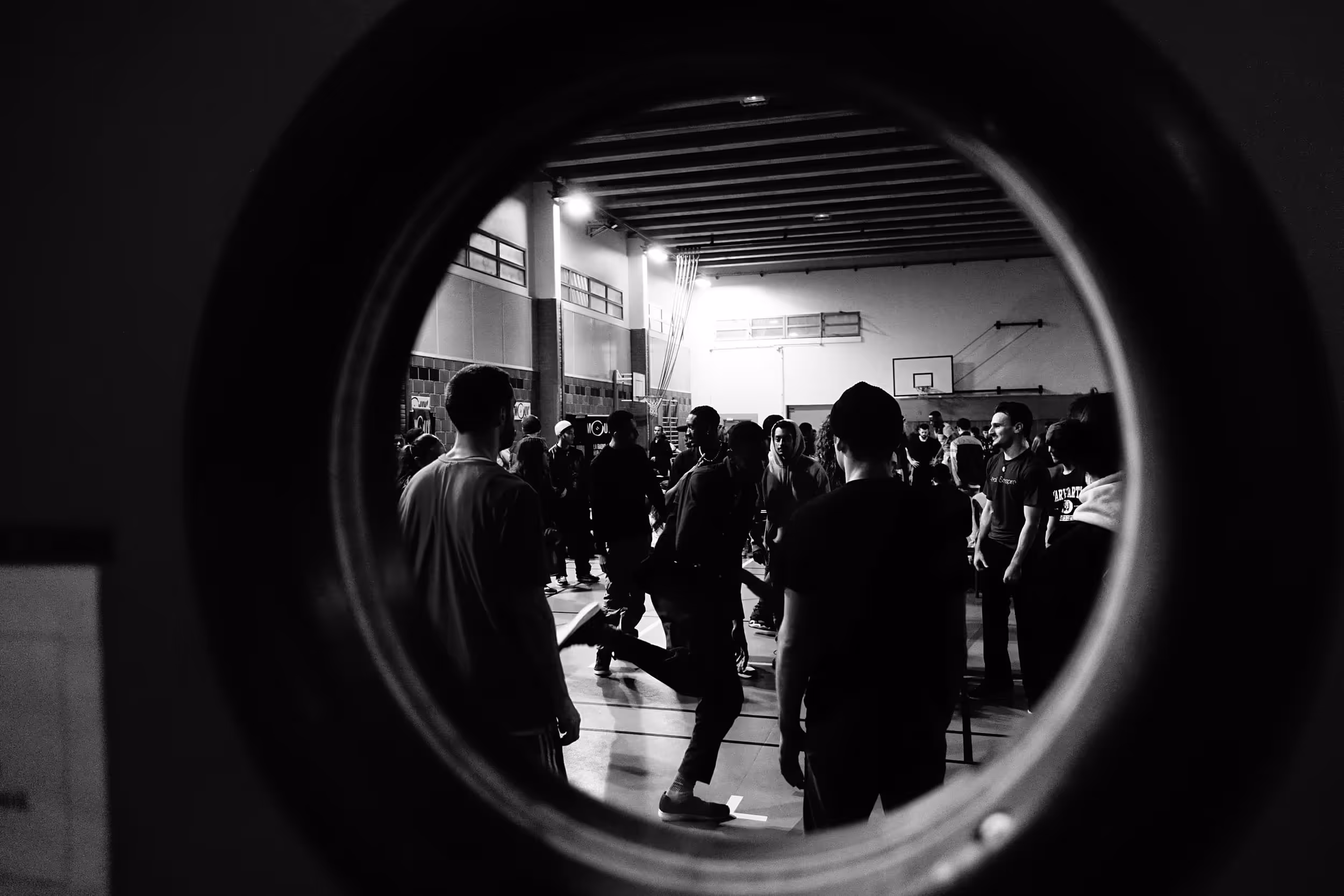 Vue à travers un hublot circulaire d'une salle de danse animée, avec des participants en pleine interaction.