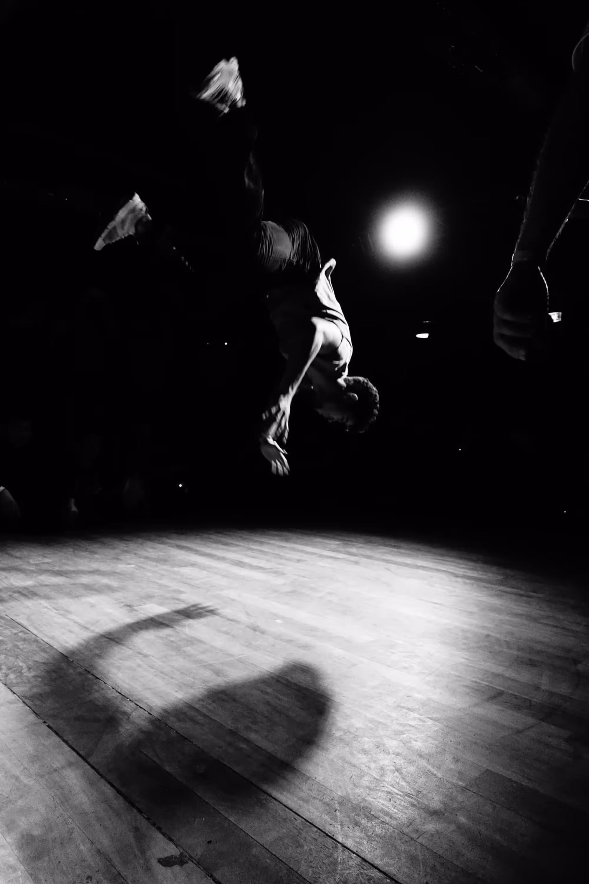Danseur en plein saut acrobatique, silhouette figée dans les airs avec un fort jeu d’ombres au sol.