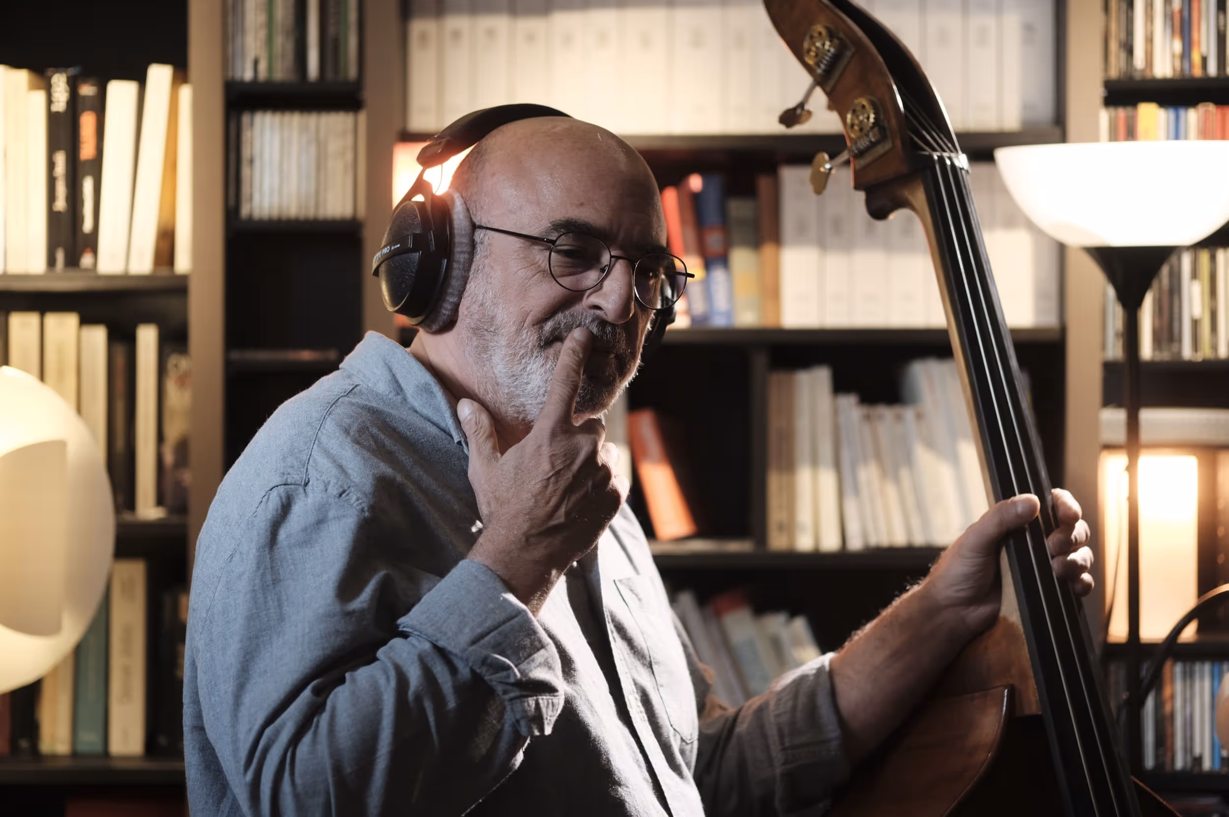 Homme âgé jouant de la contrebasse avec un casque audio, entouré de livres.