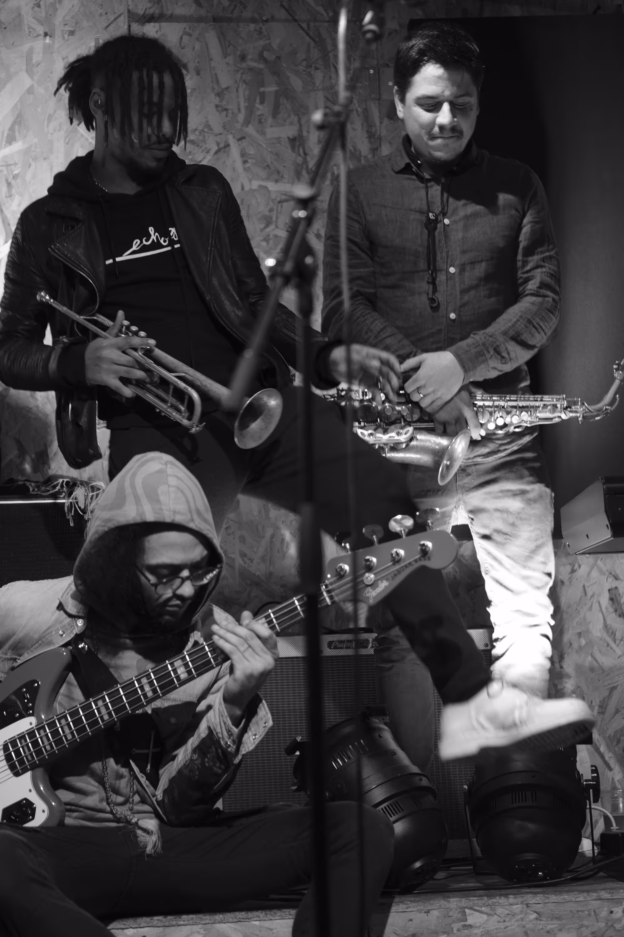 Groupe de musiciens improvisant sur scène avec guitare basse, saxophone et trompette.