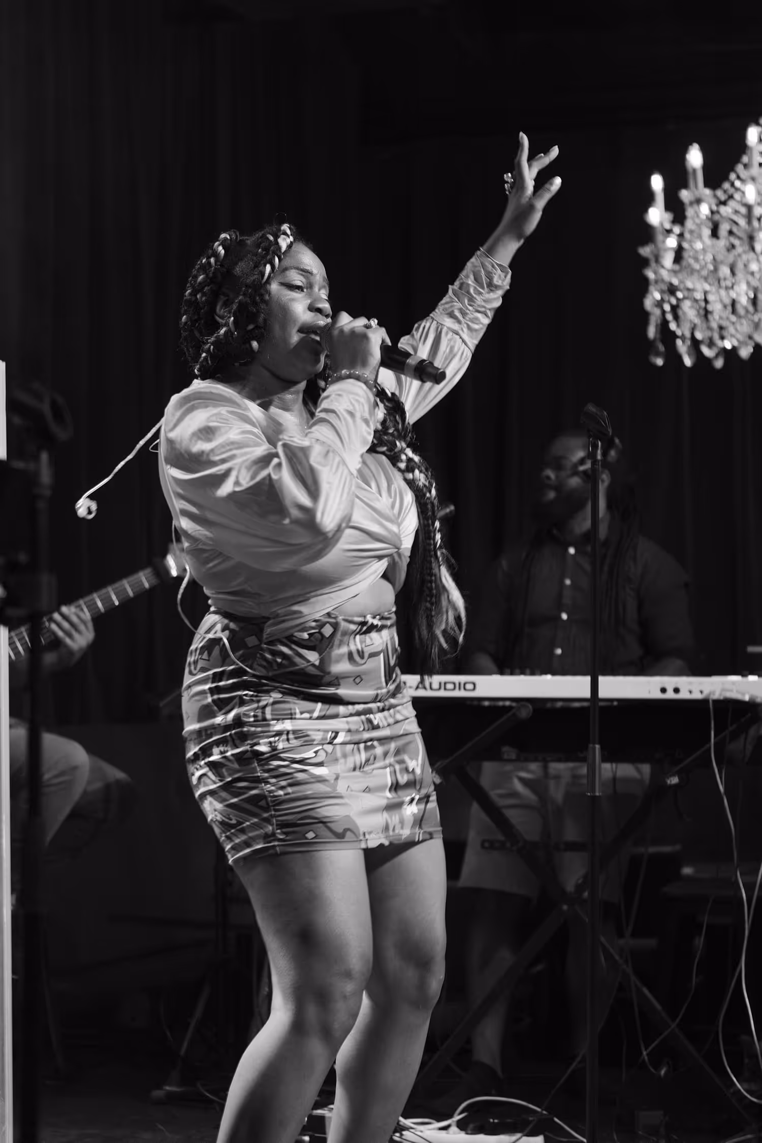 Chanteuse en pleine performance sur scène avec micro, accompagnée par un musicien au clavier en arrière-plan.