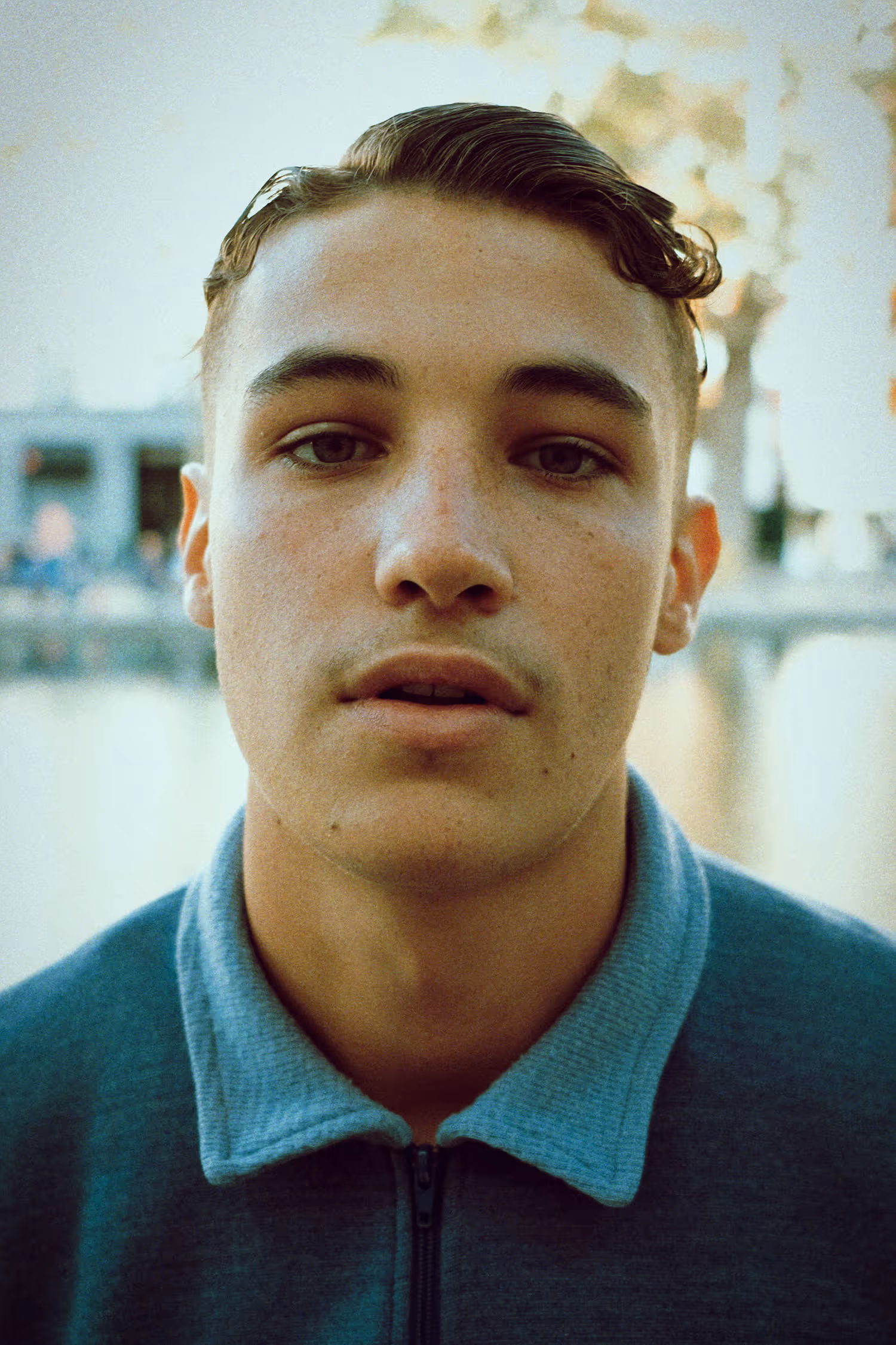 Portrait rapproché d'un jeune homme aux cheveux courts coiffés en arrière portant un sweat à col zippé bleu.