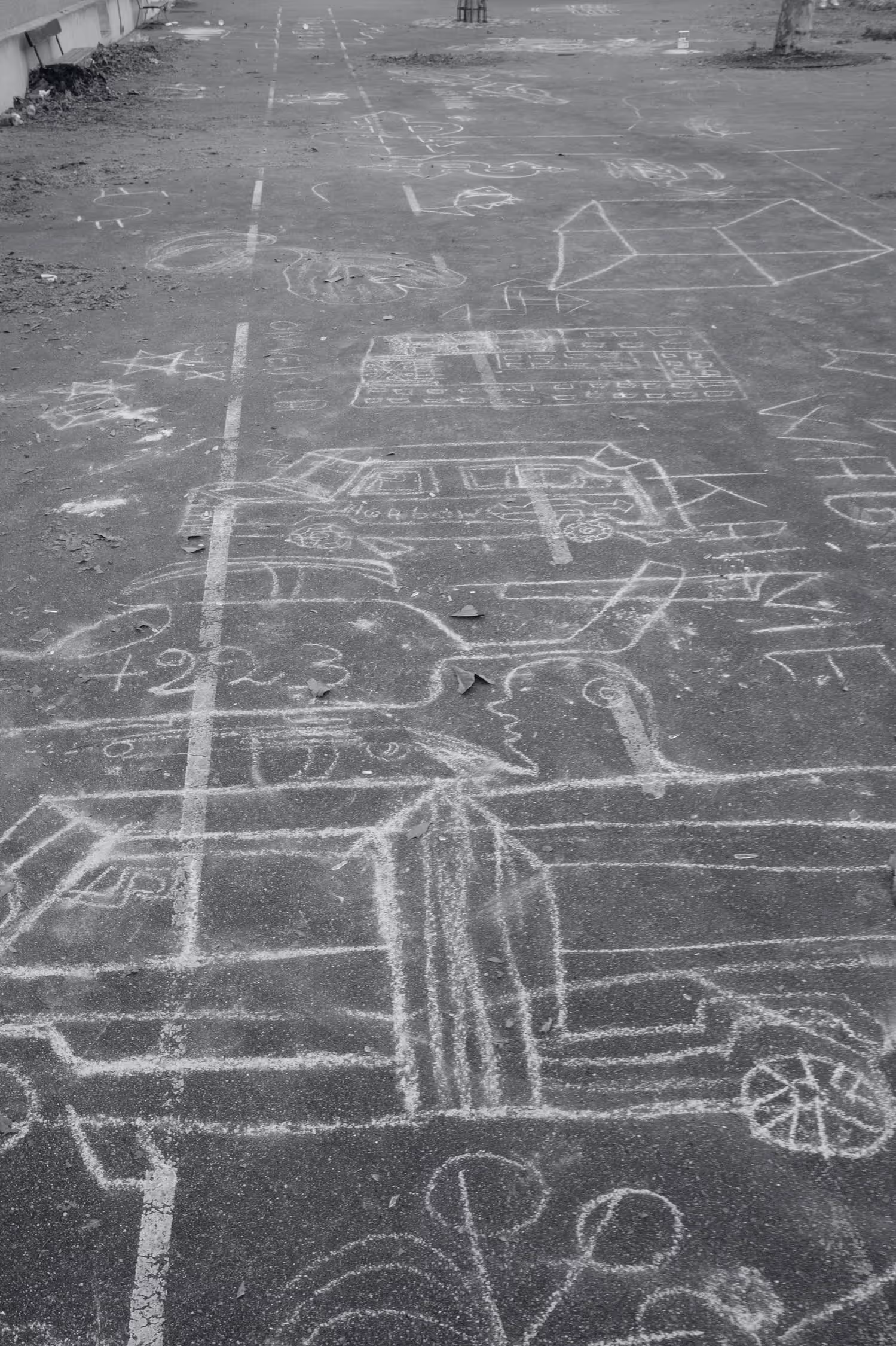 Dessin à la craie blanche sur le sol d'une cour, représentant des voitures, un bus, des formes géométriques, un visage, des étoiles et divers symboles.