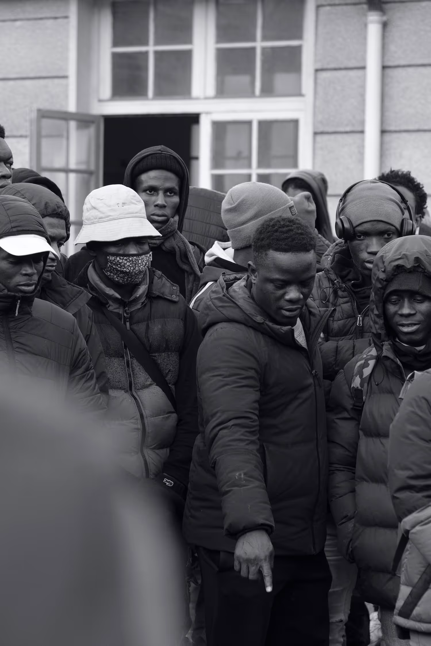 Groupe d'hommes portant des vêtements d'hiver devant un bâtiment, certains avec des capuches et un masque facial.