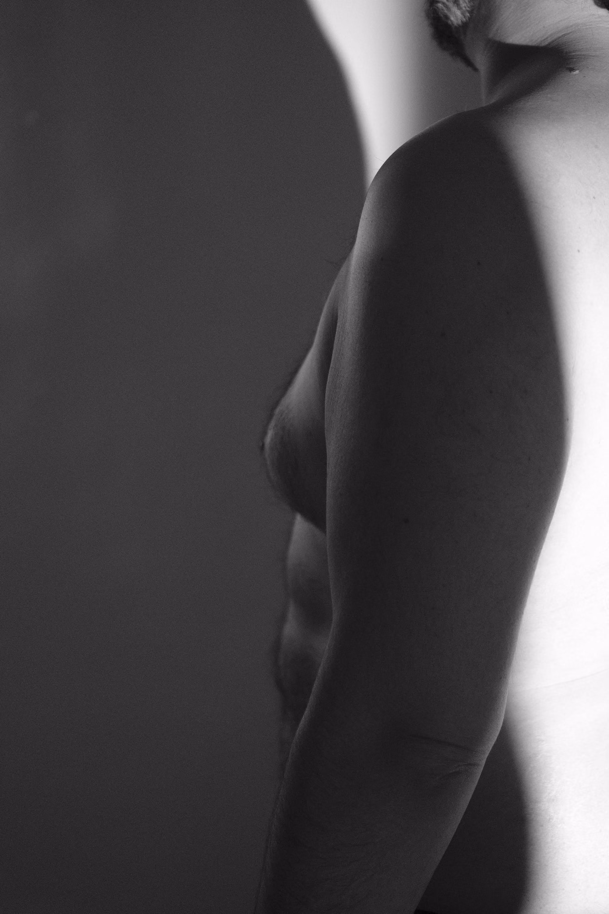 Gros plan en noir et blanc d’un torse masculin nu avec un jeu d’ombre et lumière.